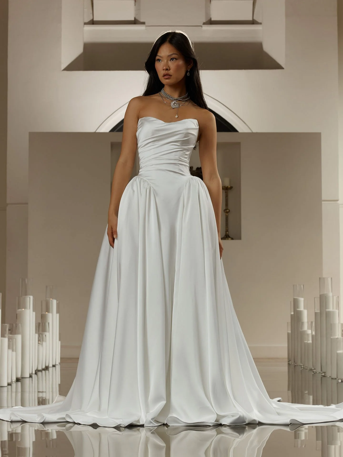 Model wearing an Evie Young strapless satin ballgown wedding dress featuring an elegantly draped bodice, a dropped basque waistline, and a voluminous pleated skirt