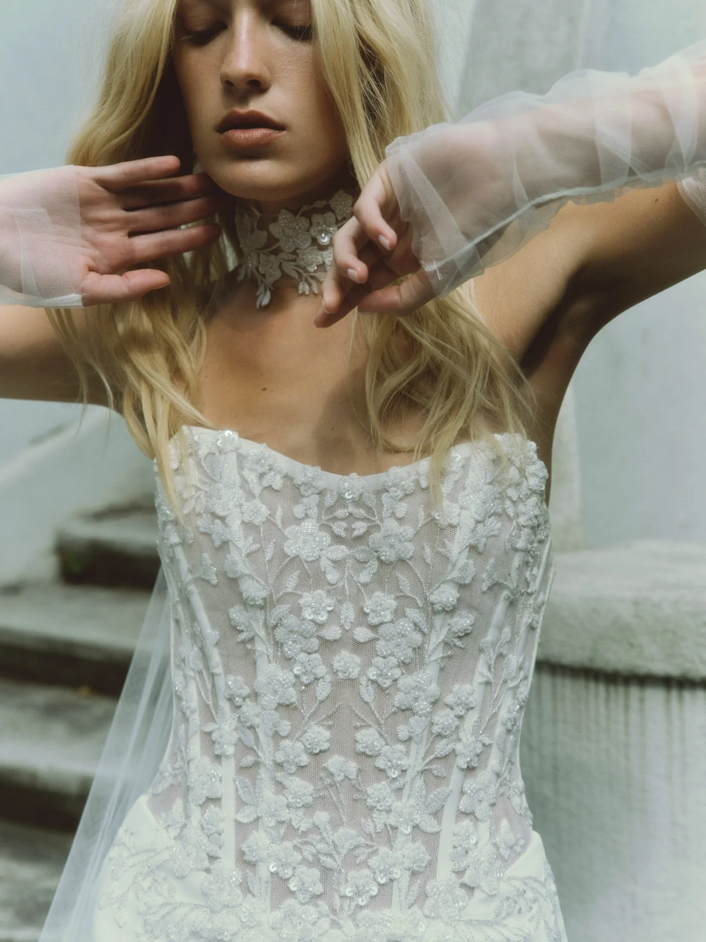 Close-up of a model wearing a Rivini strapless wedding dress showcasing a sheer corset bodice with intricate 3D floral beadwork, styled with a matching floral choker and sheer tulle gloves.