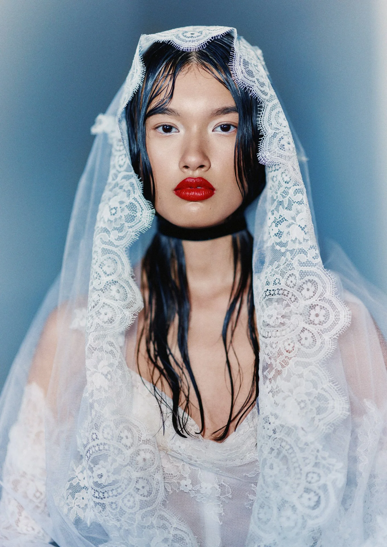 Close-up portrait of a model wearing a delicately scalloped Former Girlfriend lace mantilla bridal veil draped over her head, styled with a black ribbon choker and bold red lipstick.