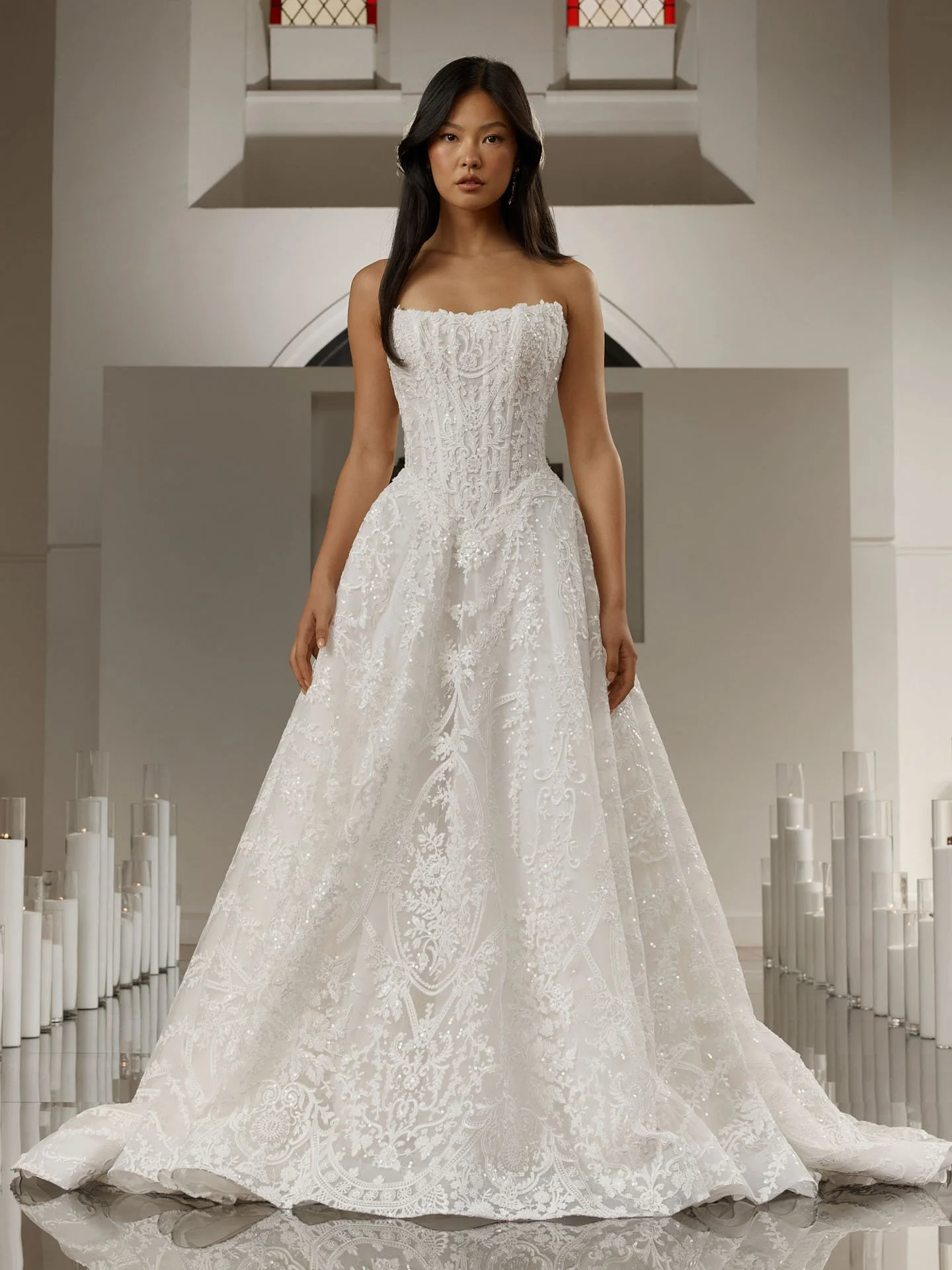 Model wearing a strapless Evie Young lace ballgown wedding dress featuring a straight neckline, a highly structured basque waist corset, and a full skirt with elaborate all-over beadwork.