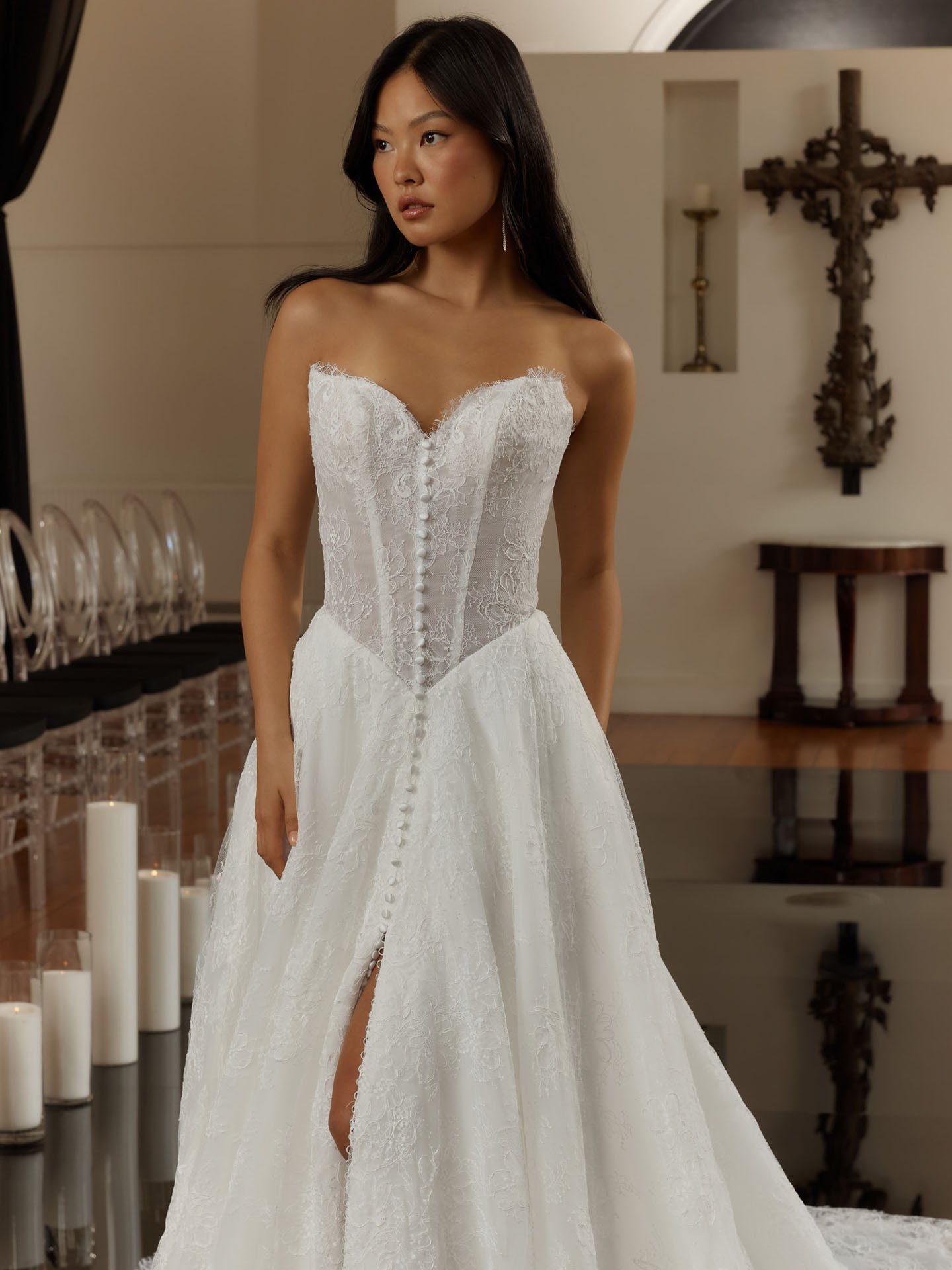 Model wearing an Evie Young strapless lace wedding dress featuring a sheer corset bodice, eyelash lace trim along a sweetheart neckline, delicate front buttons, and a high leg slit.