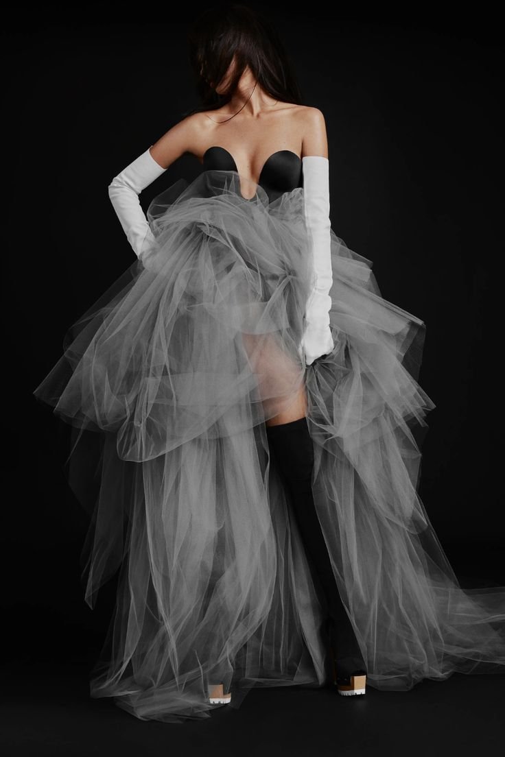 Model wearing an avant-garde Vera Wang wedding dress featuring a contrasting black sweetheart bodice with a deep plunge and a massive, voluminous grey tulle high-low skirt, styled with white opera gloves and black thigh-high boots.
