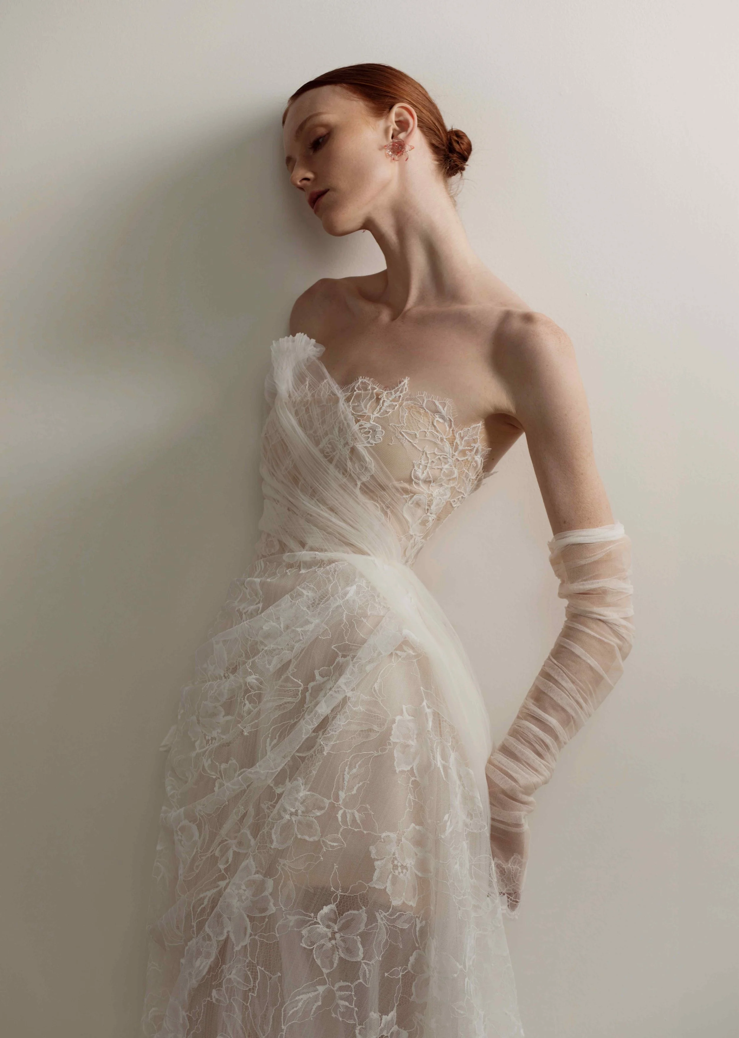 Model wearing an OUMA strapless wedding dress featuring a lace bodice asymmetrically draped with sheer tulle, paired with matching ruched sheer tulle opera sleeves.