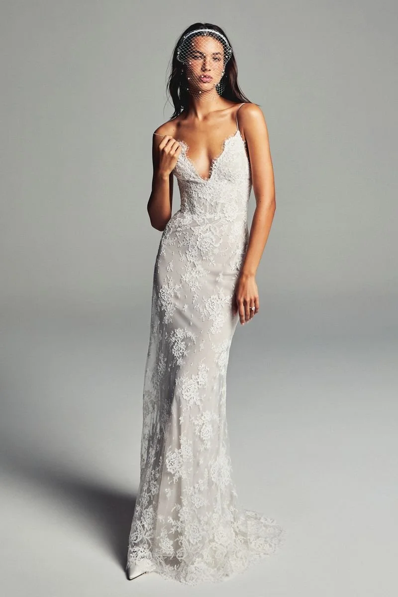 Model wearing a Monique Lhuillier V-neck lace fitted sheath wedding dress with delicate spaghetti straps, intricate floral embroidery, a sweep train, and a beaded birdcage veil.