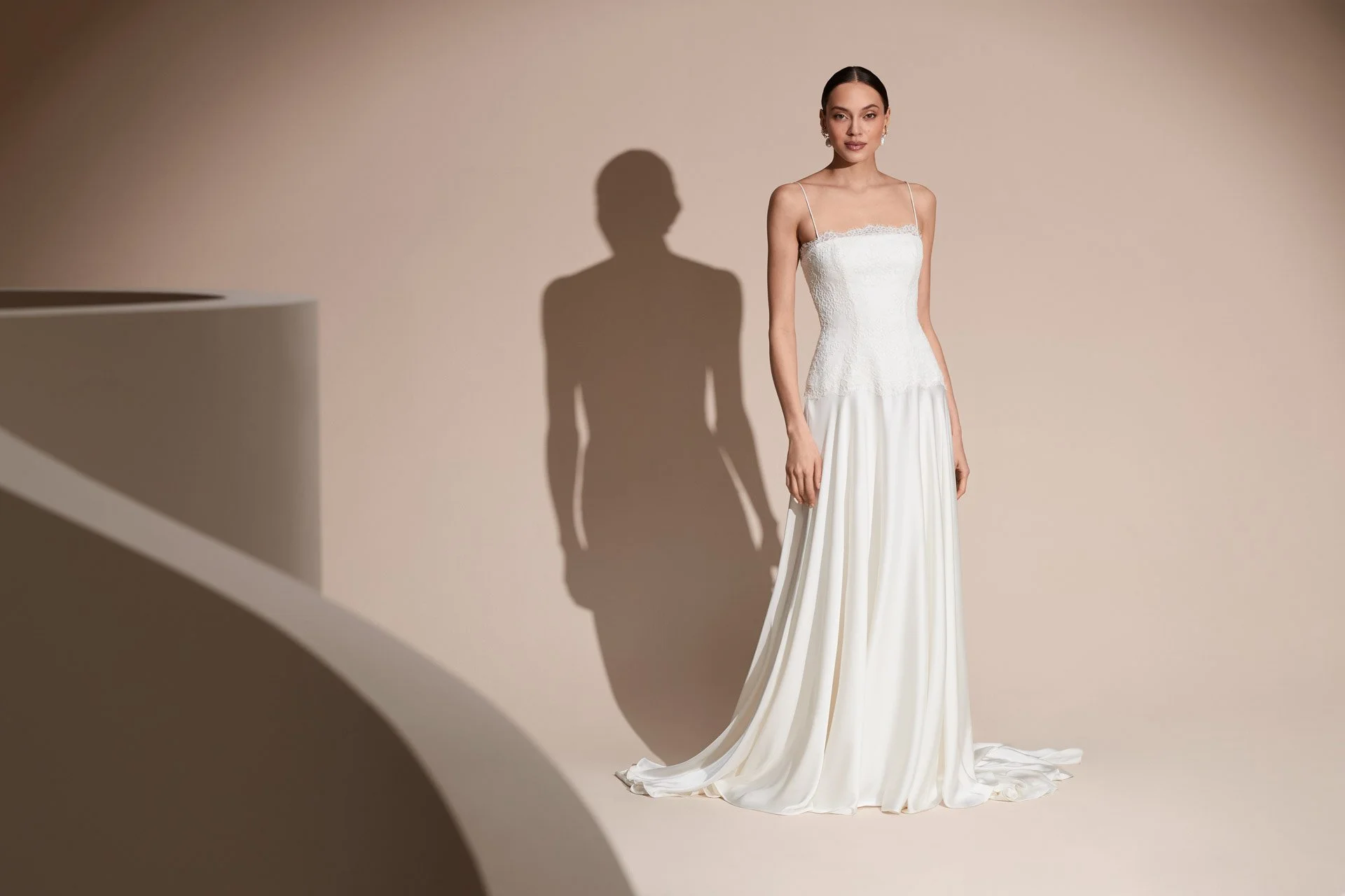 Model wearing a Savannah Miller wedding dress featuring delicate spaghetti straps, a fitted lace corset bodice with subtle scalloped trim, and a flowing white silk skirt with a sweeping train.