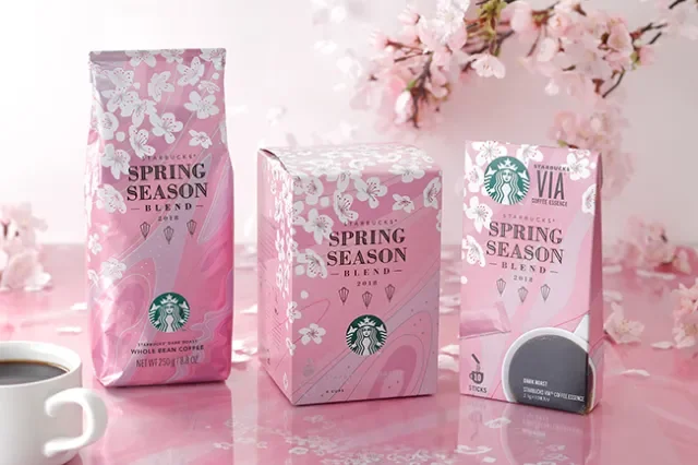 Starbucks Spring Season coffee products on pink surface, with a cup of coffee and cherry blossoms in background.