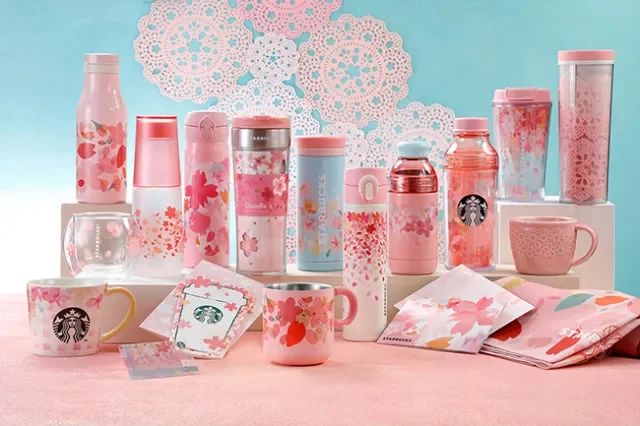 Collection of pink and white Starbucks beverage bottles and cups with cherry blossom designs, set against a pastel background with lace decorations.