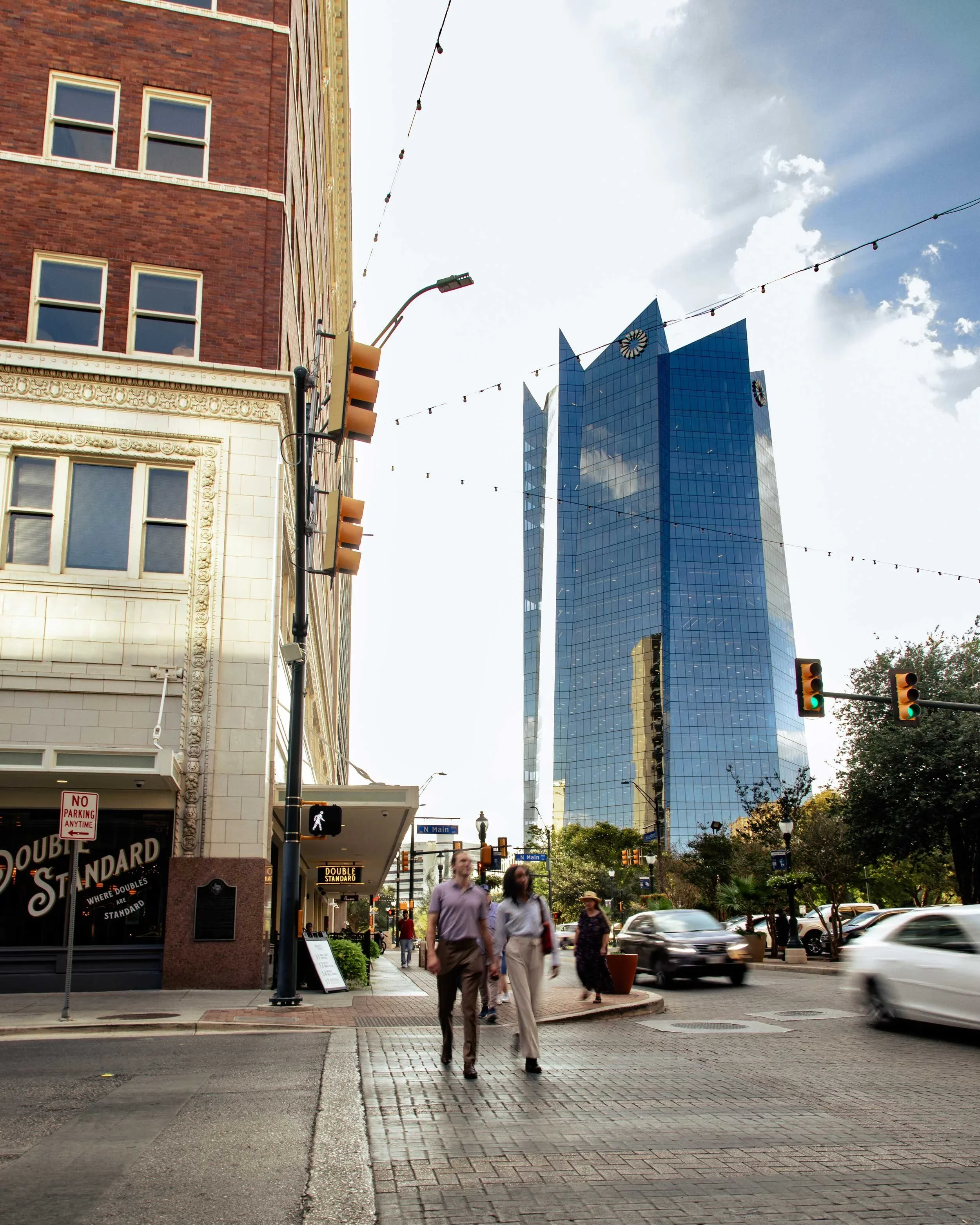 City street scene with pedestrians, cars, a red brick building with decorative details, a store sign for Double Standard, and tall blue glass skyscraper in the background.