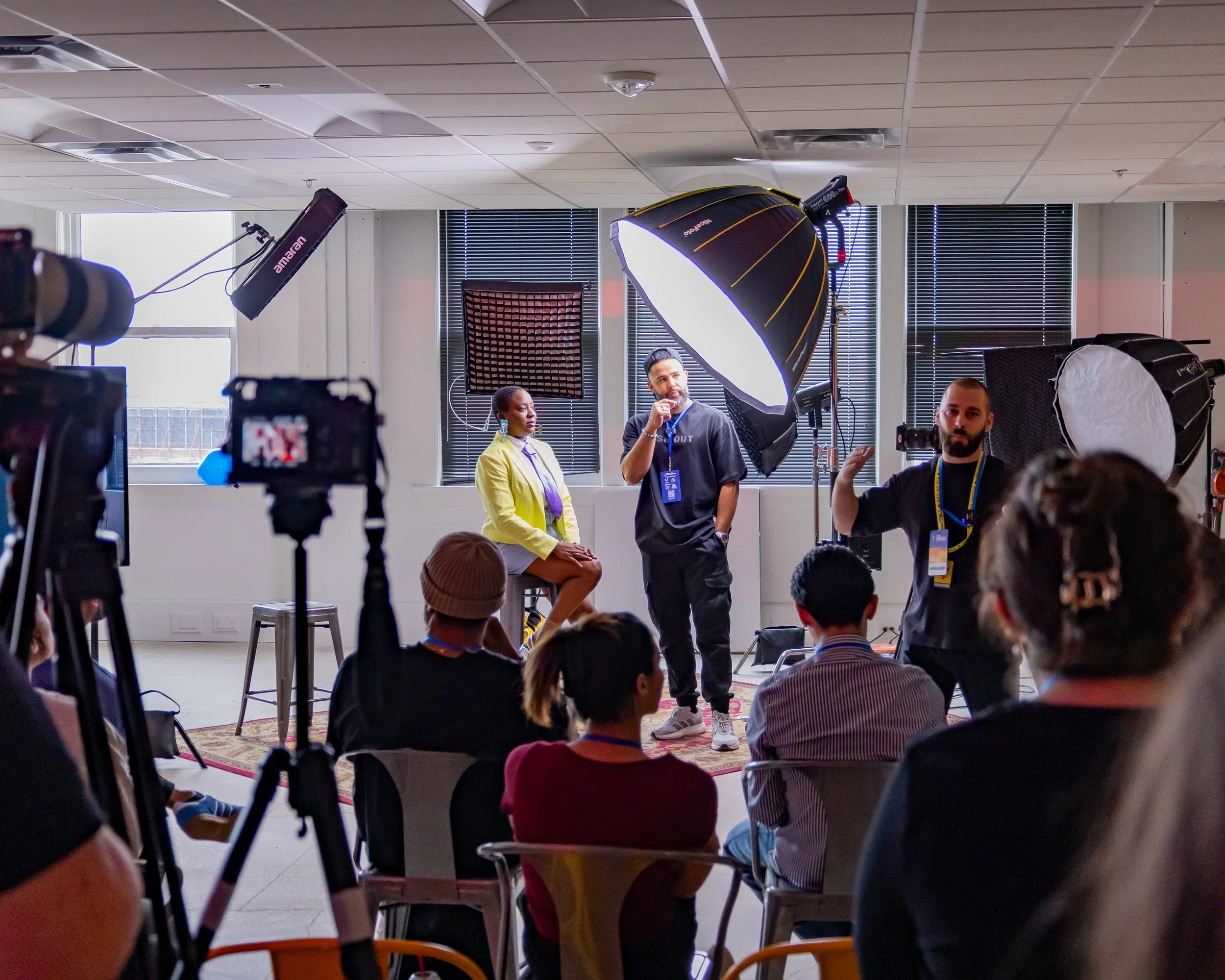 People participating in a panel discussion or interview in a conference room with professional lighting equipment set up.