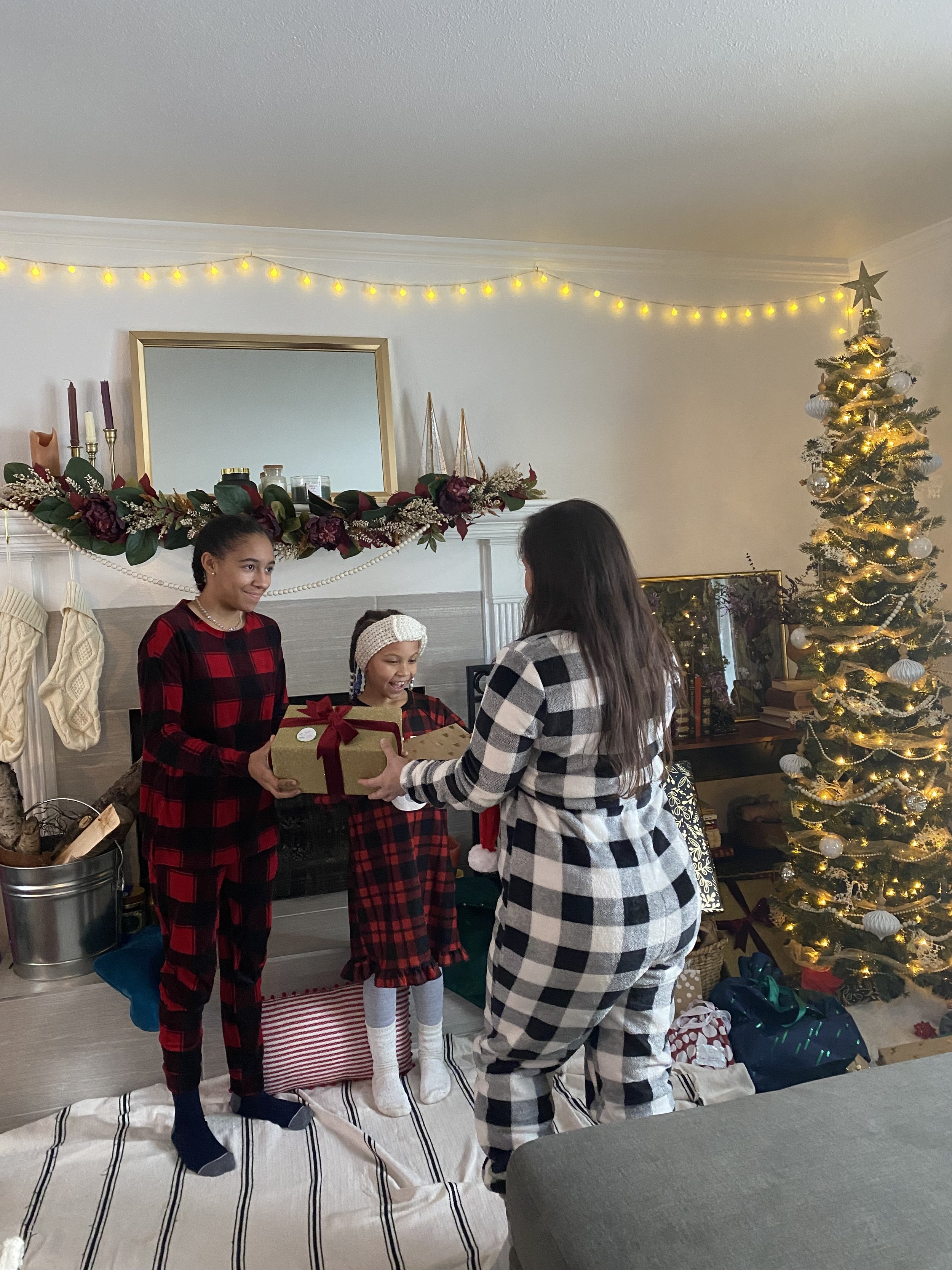 Mom and kids exchanging gifts in a festively decorated living room with a Christmas tree, stockings, and holiday decorations.