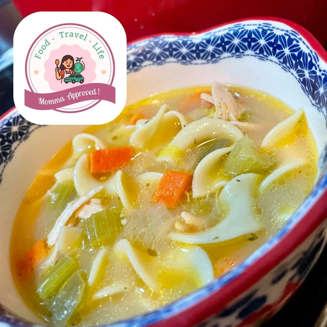 A bowl of chicken noodle soup with carrots, celery, and shredded chicken in a clear broth, served in a decorative ceramic bowl.