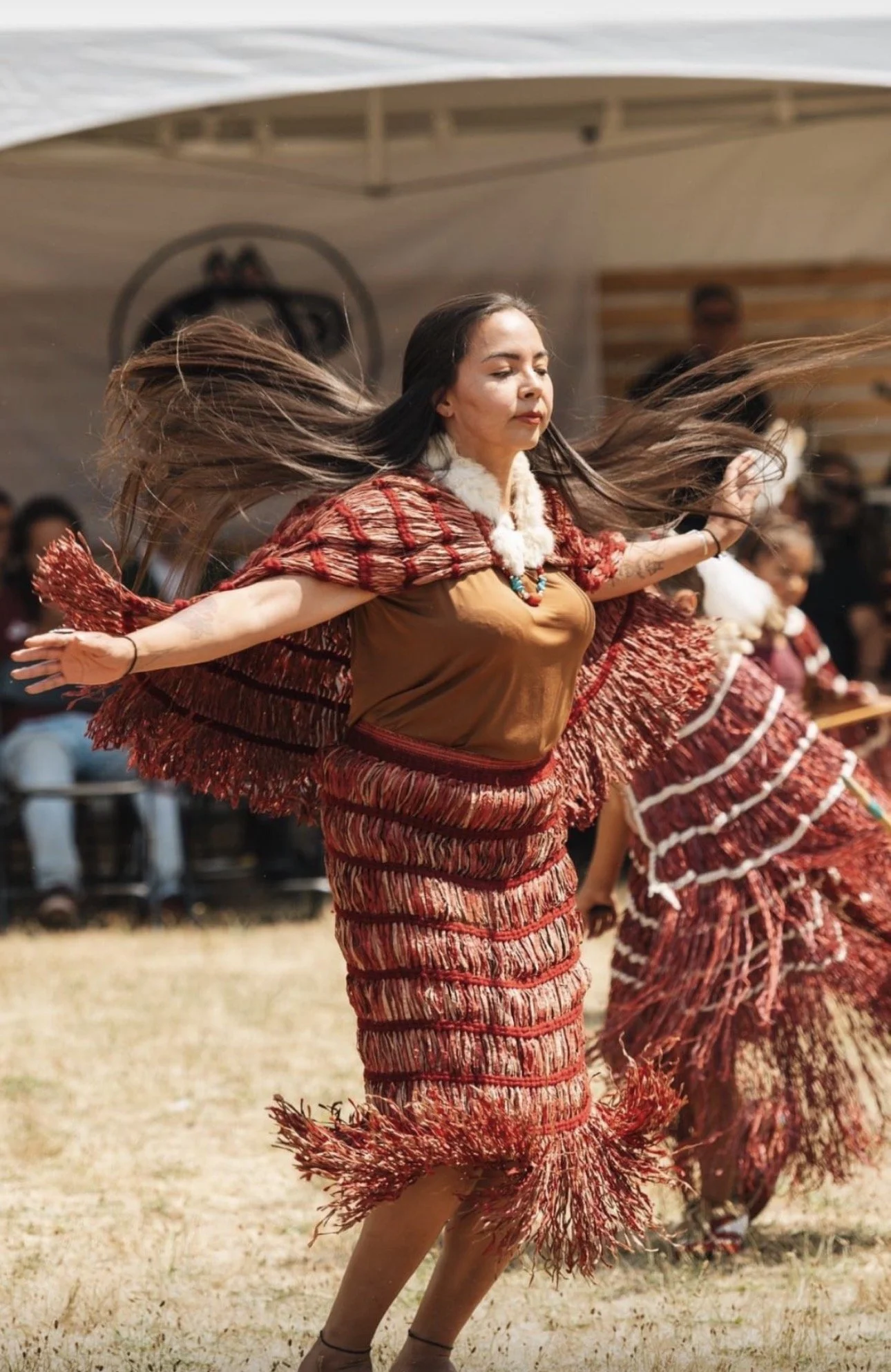 A woman in traditional Indigenous attire dancing with her arms outstretched and her hair flowing in motion during a cultural event.