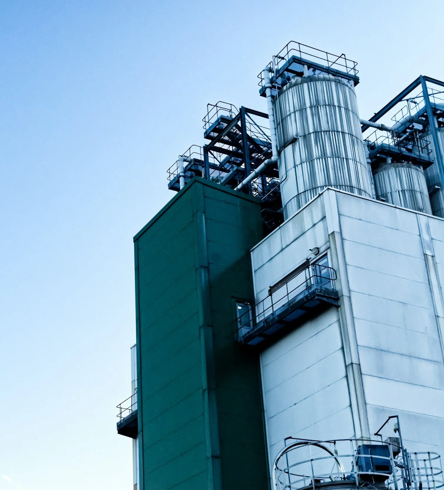 Side view of an industrial building with large metal tanks and external staircases against a clear sky.