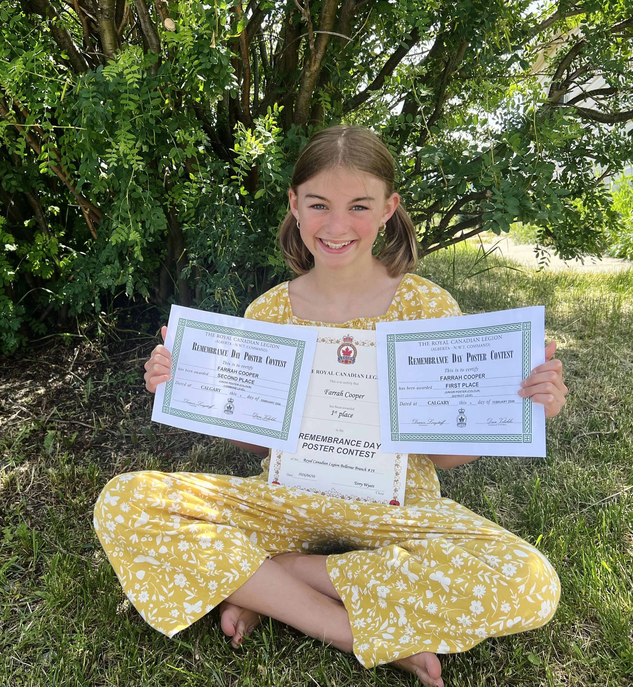 A girl with blond hair showing three art awards she has received for her Remembrance day Poster