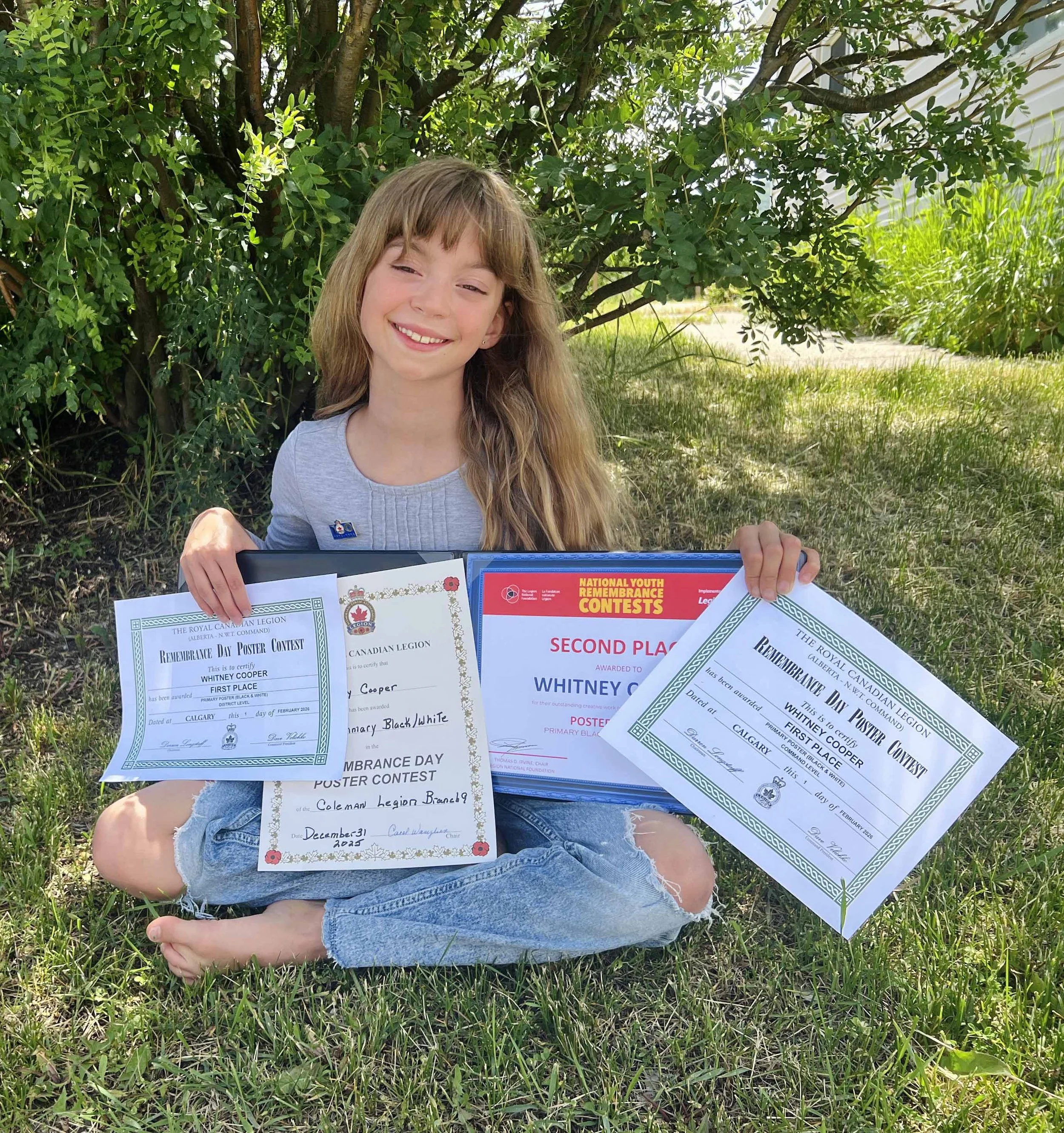 A young girl with long blond hair showing four art awards she has received for her Remembrance day Poster