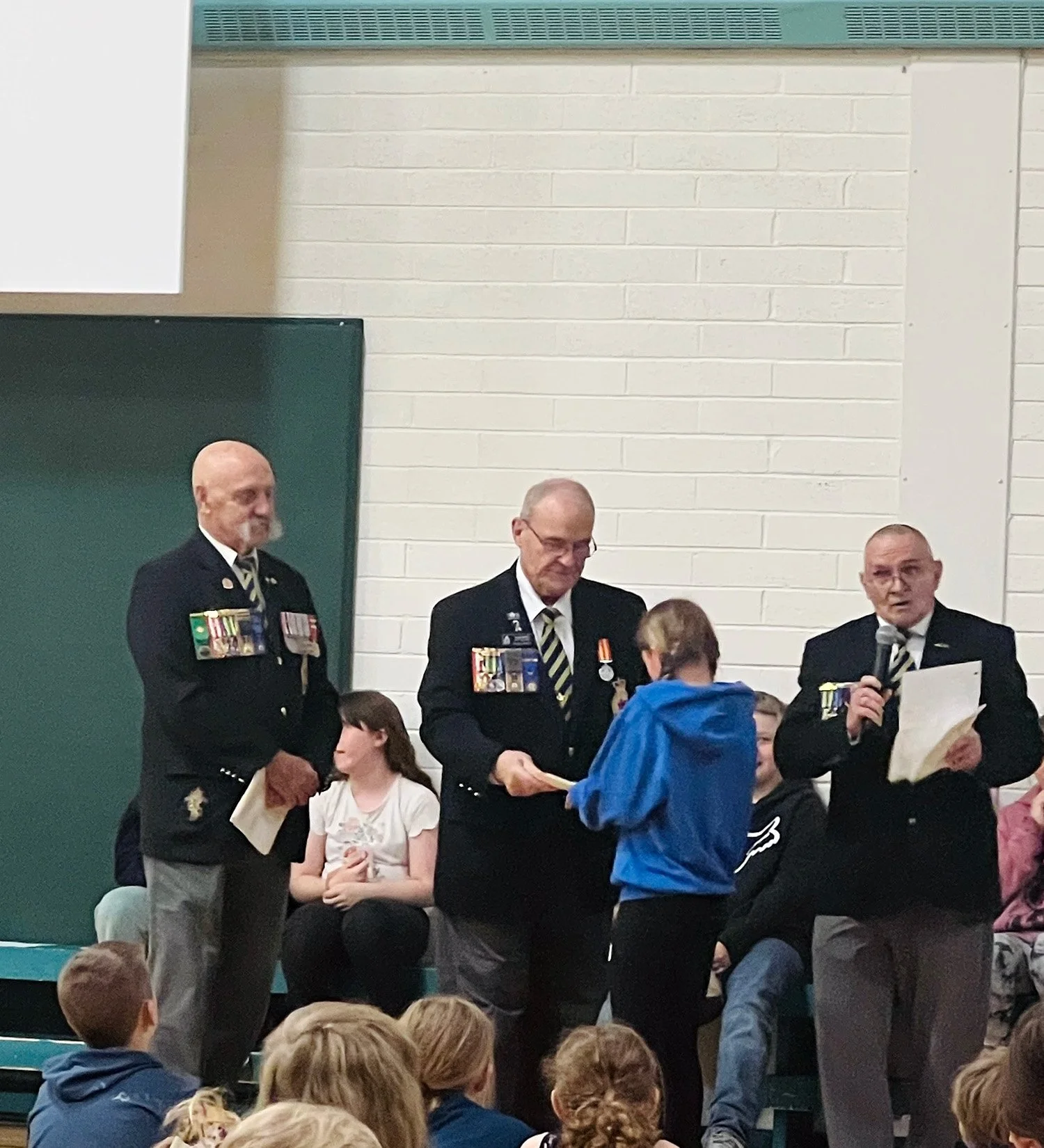 Girl receiving award from three Canadian veterans at her school