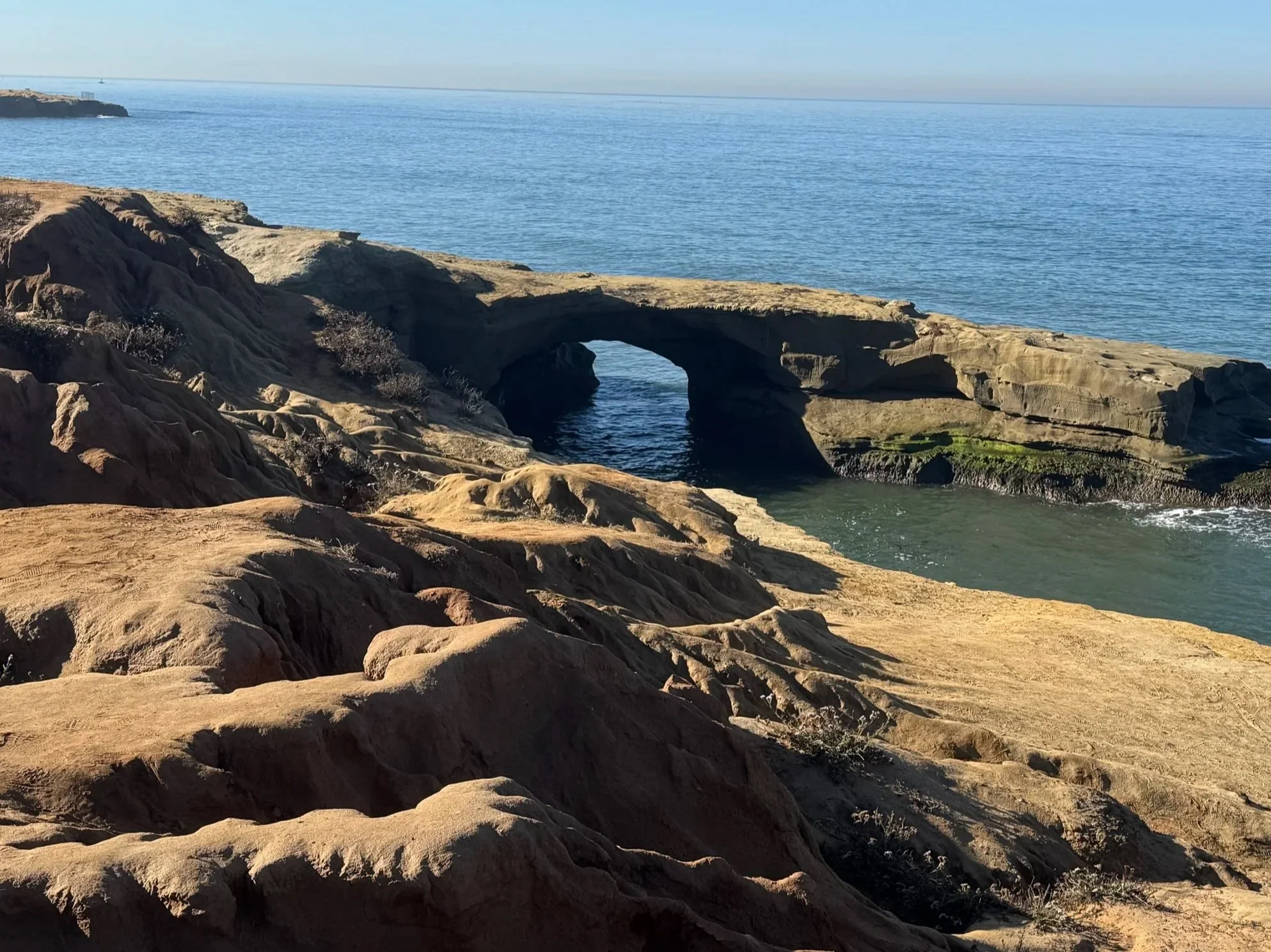 A rocky coastal landscape with arches and cliffs overlooking the ocean, under a clear blue sky.