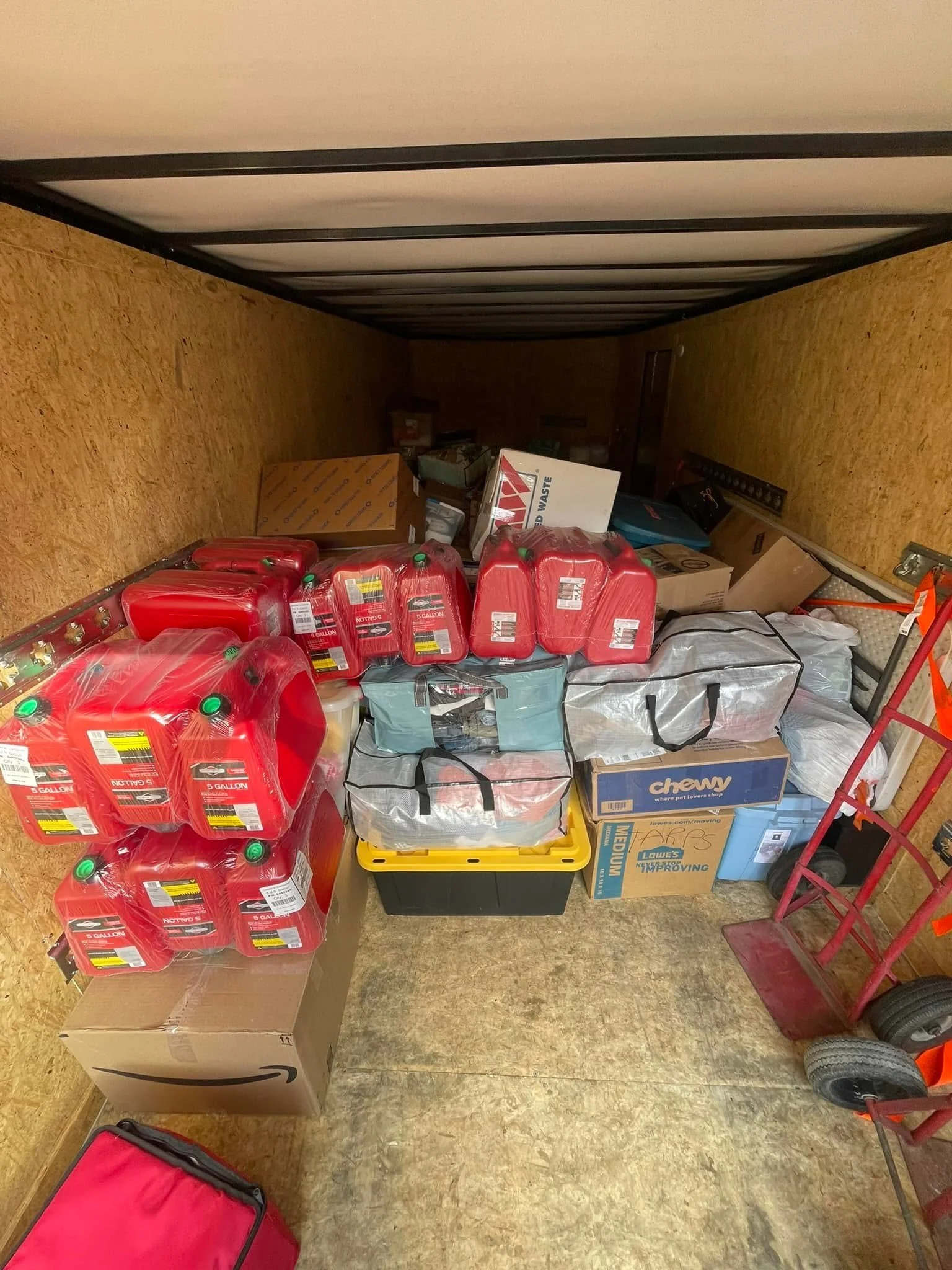 Garage storage with red gas cans, cardboard boxes, and plastic bags on the floor and shelves.