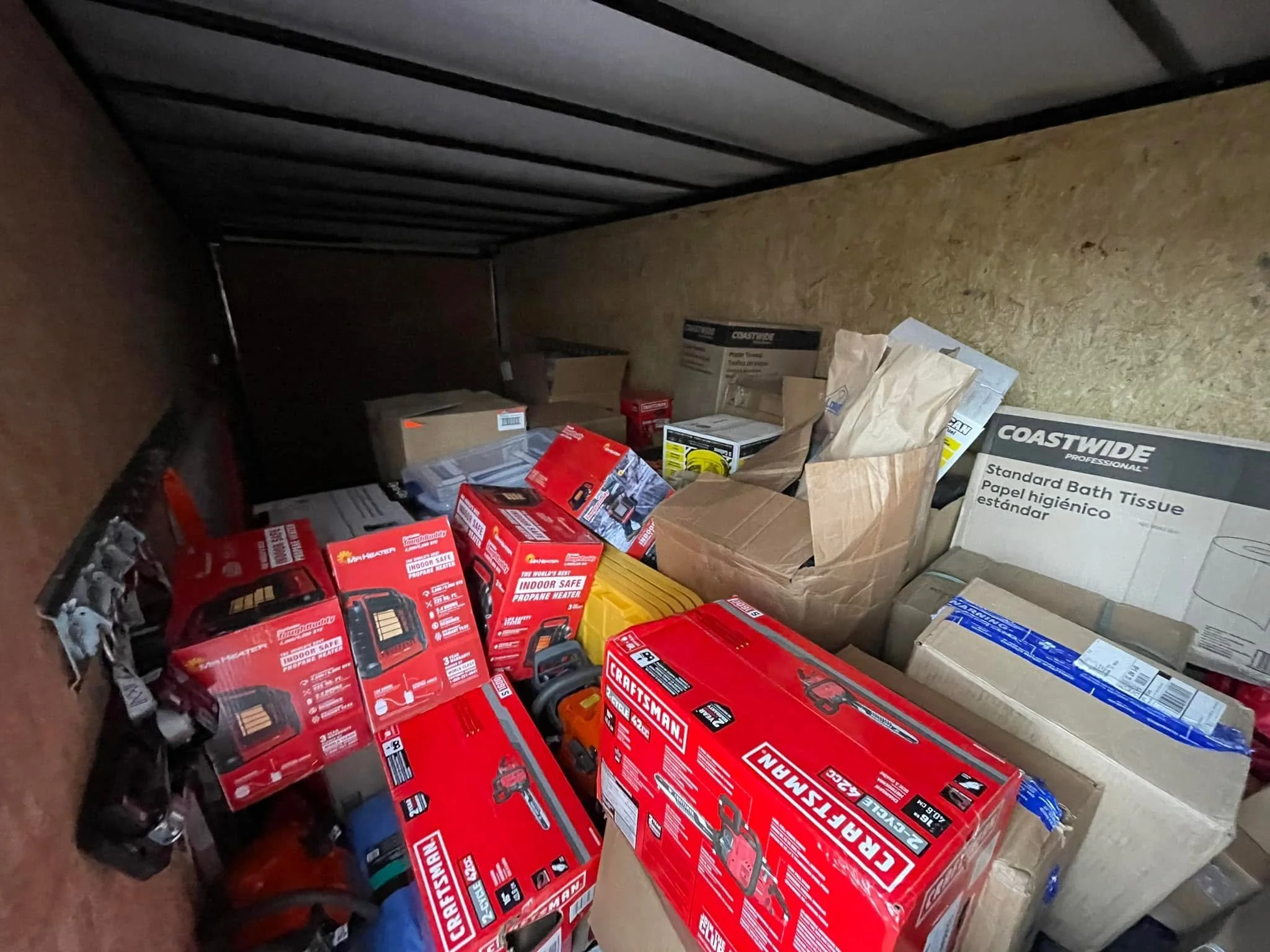 Storage area filled with boxes of tools, batteries, and household supplies, including several red boxes of Craftsman power tools, and boxes of toilet tissue paper.