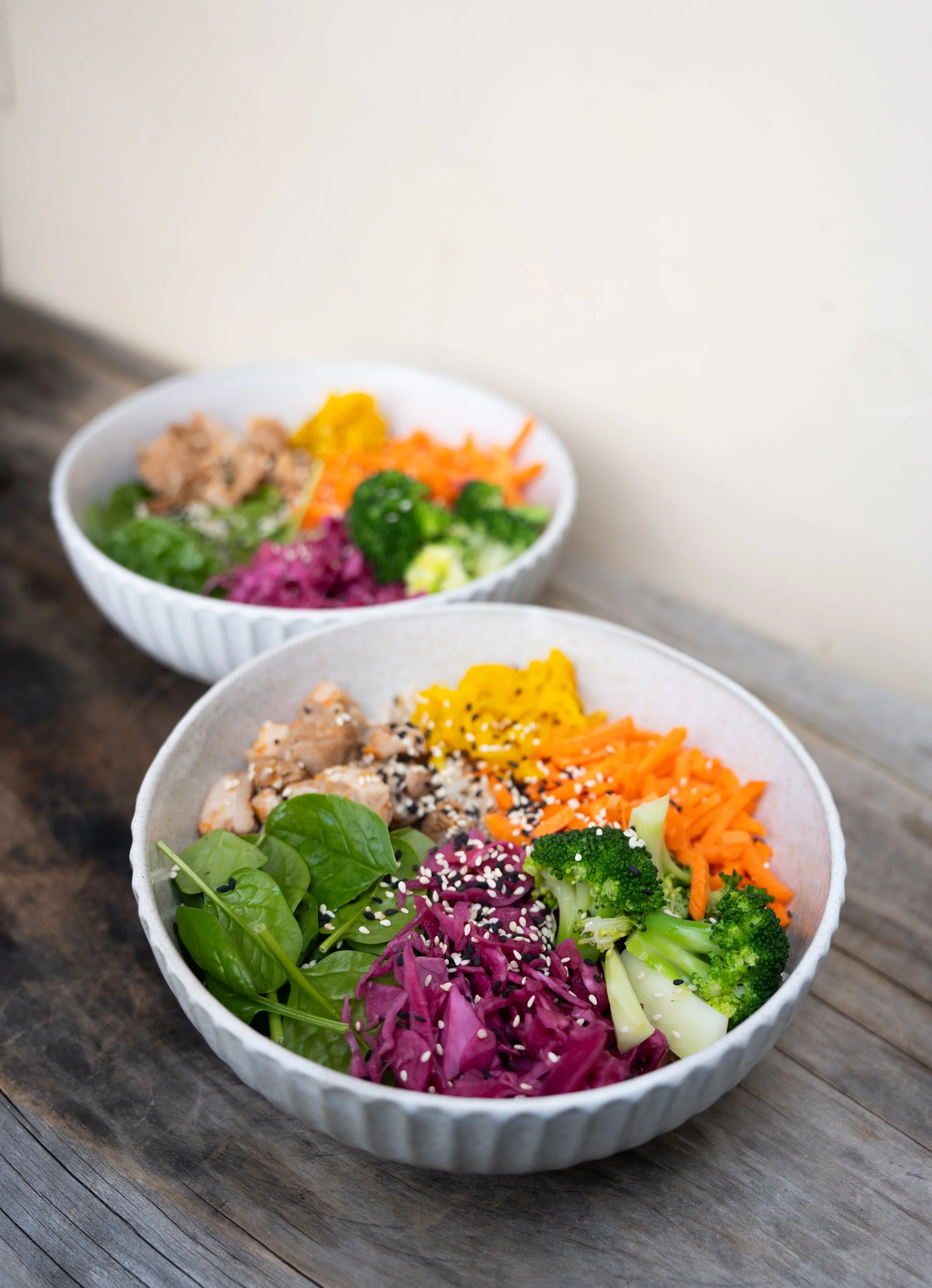 Bowls of colorful salad topped with sesame seeds on a wooden surface.