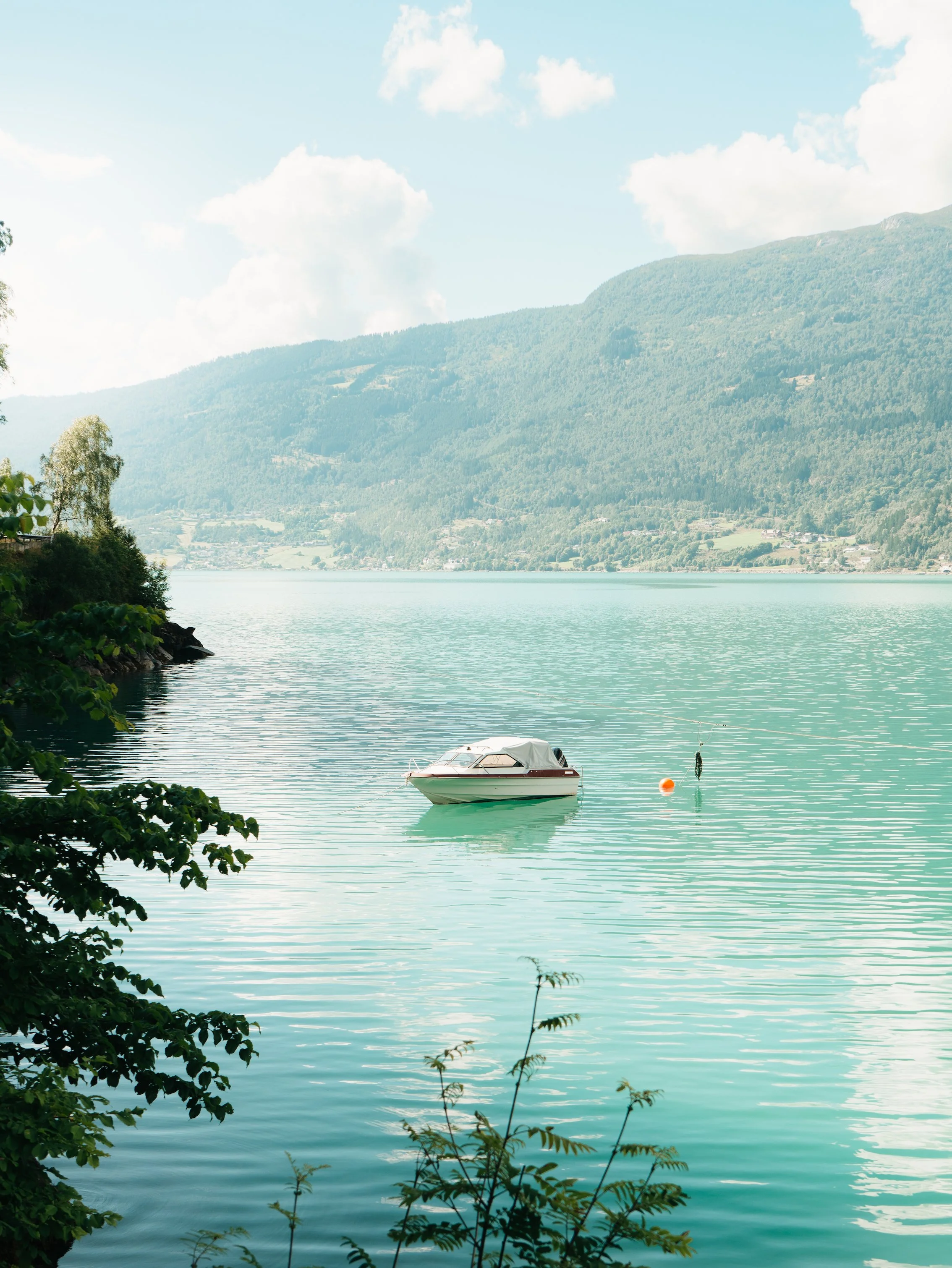 A boat floating on a calm lake with mountain scenery and partly cloudy sky in the background.