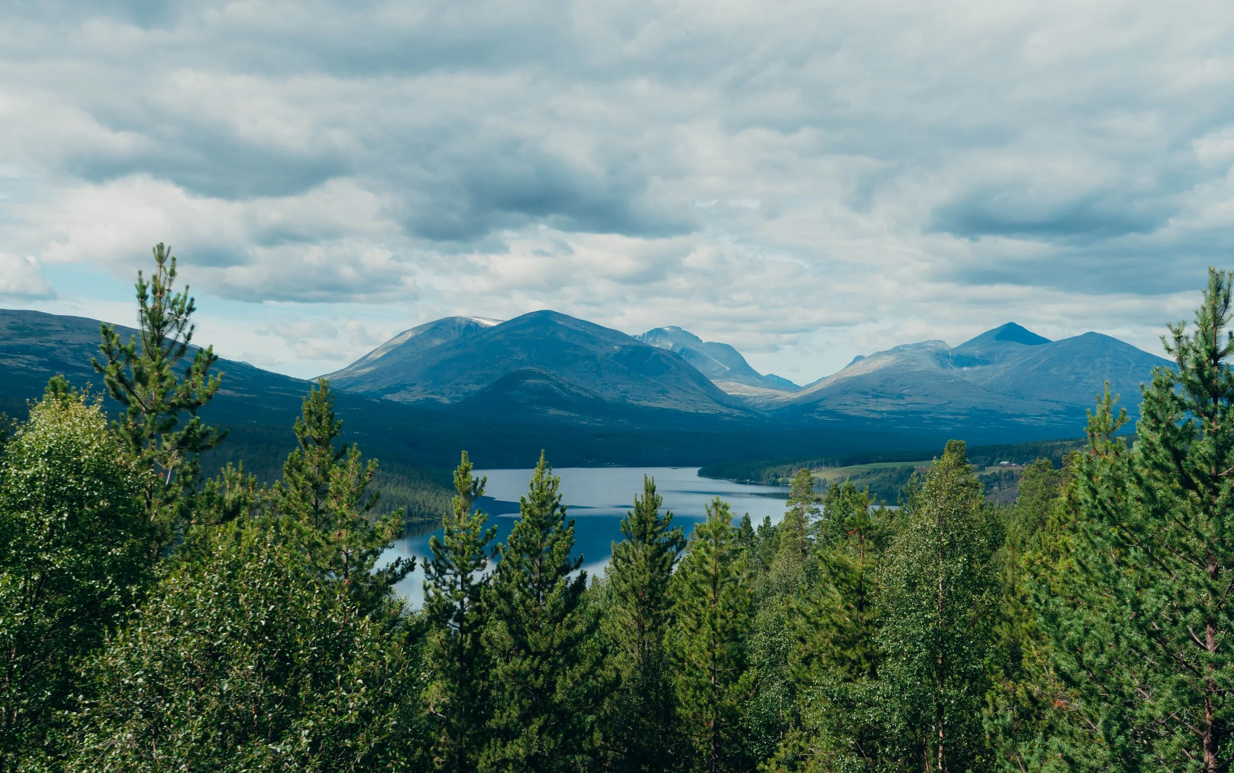 Mountain range with peaks, a lake in the foreground, and a cloudy sky.