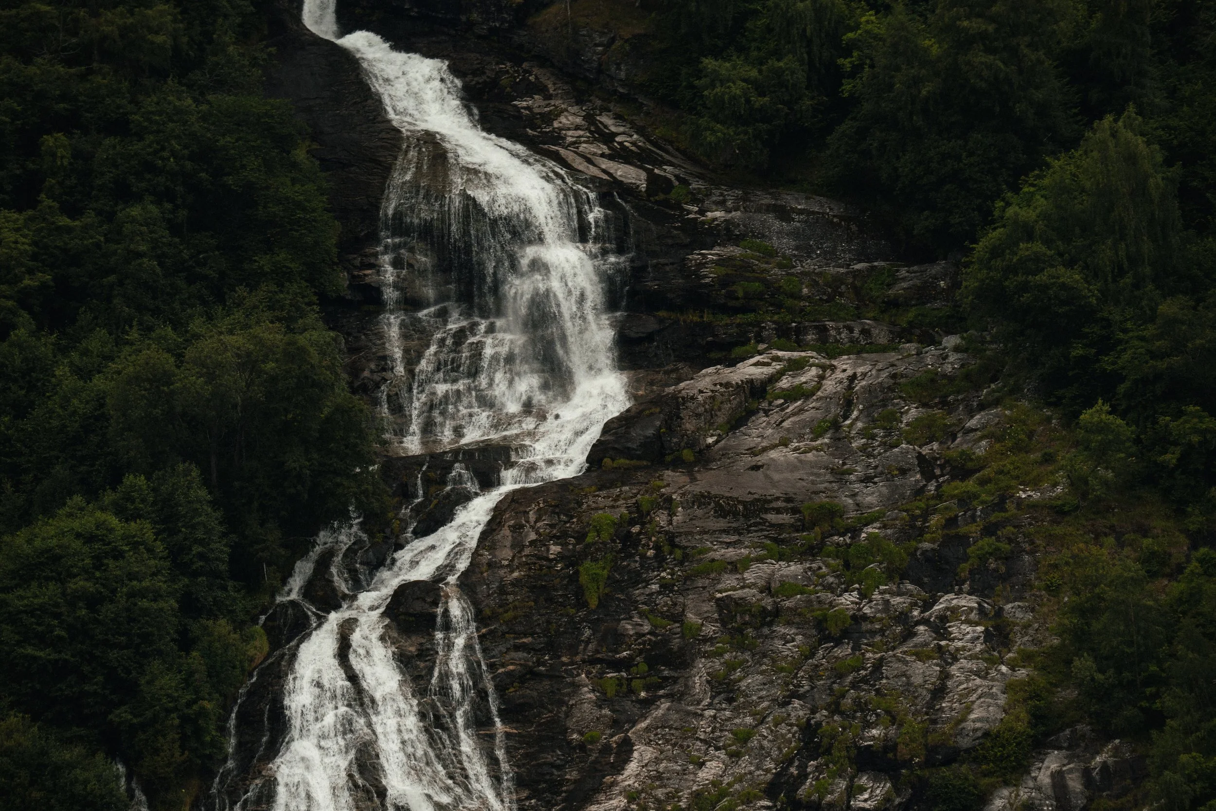 A tall, cascading waterfall flowing down a rocky mountain surrounded by dense green forest.