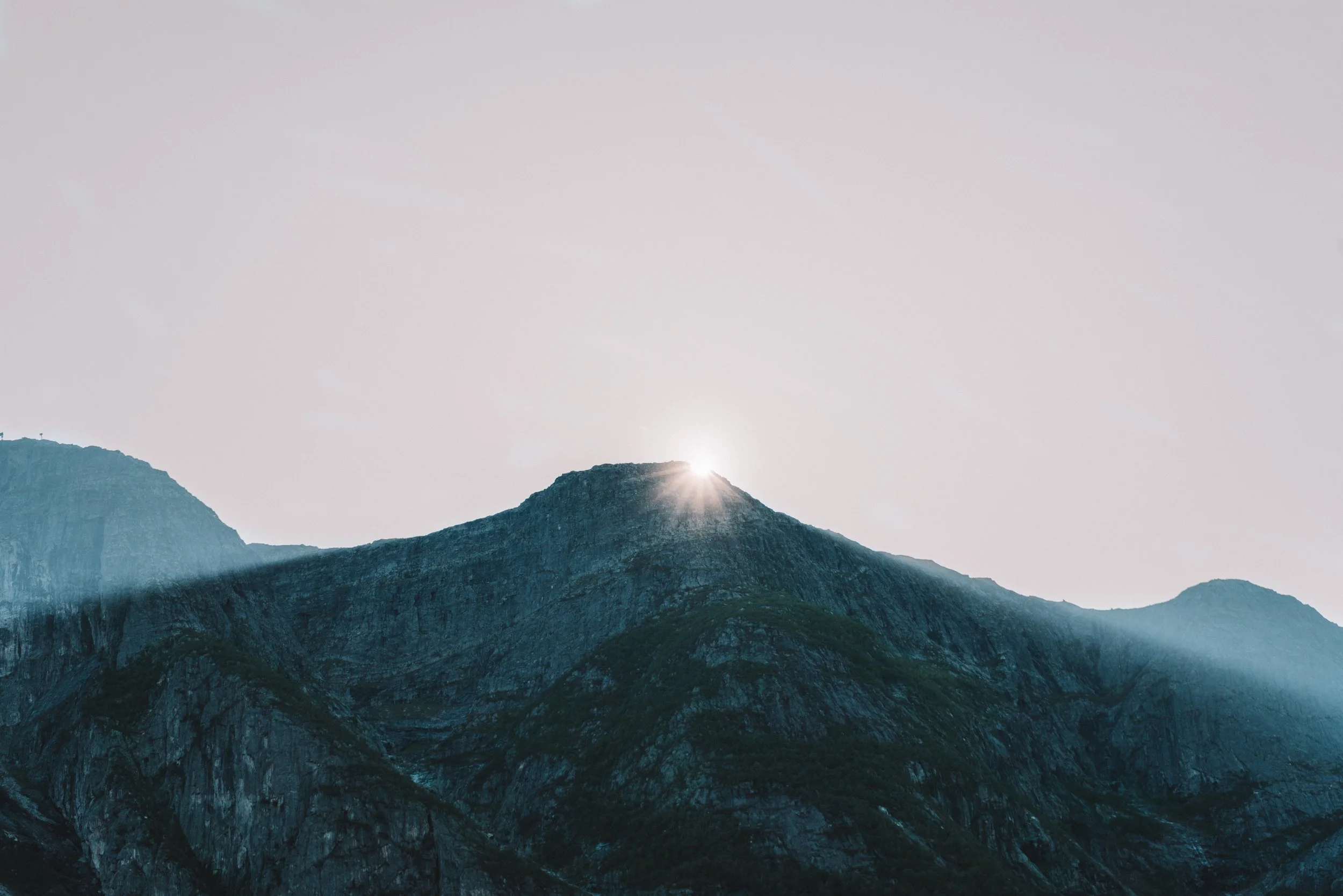 Scenic mountain landscape with sunlight peeking over the mountain peak and a clear sky.