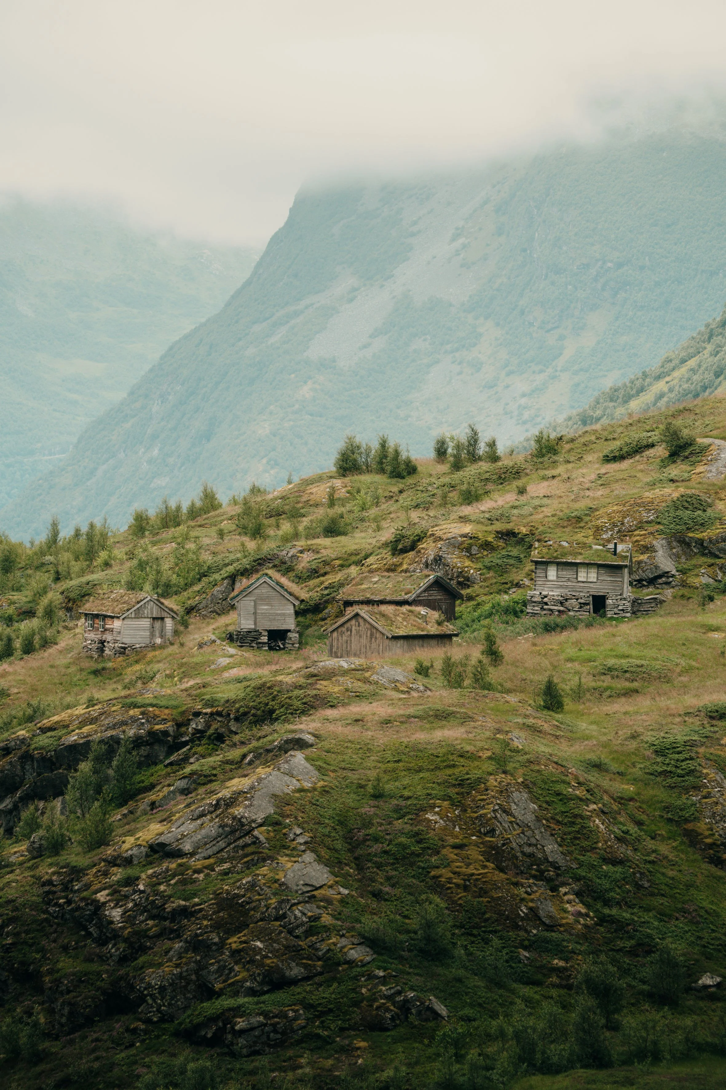 mountain landscape with foggy peaks, green slopes, and small wooden houses at the base.