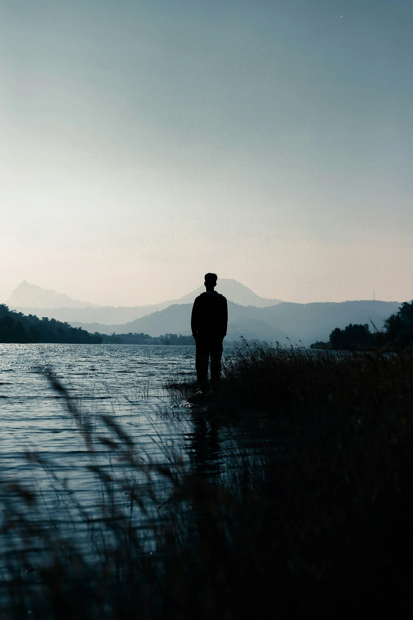 Silhouette of a person standing alone by a lake at dusk, reflecting the weight of anxiety and depression