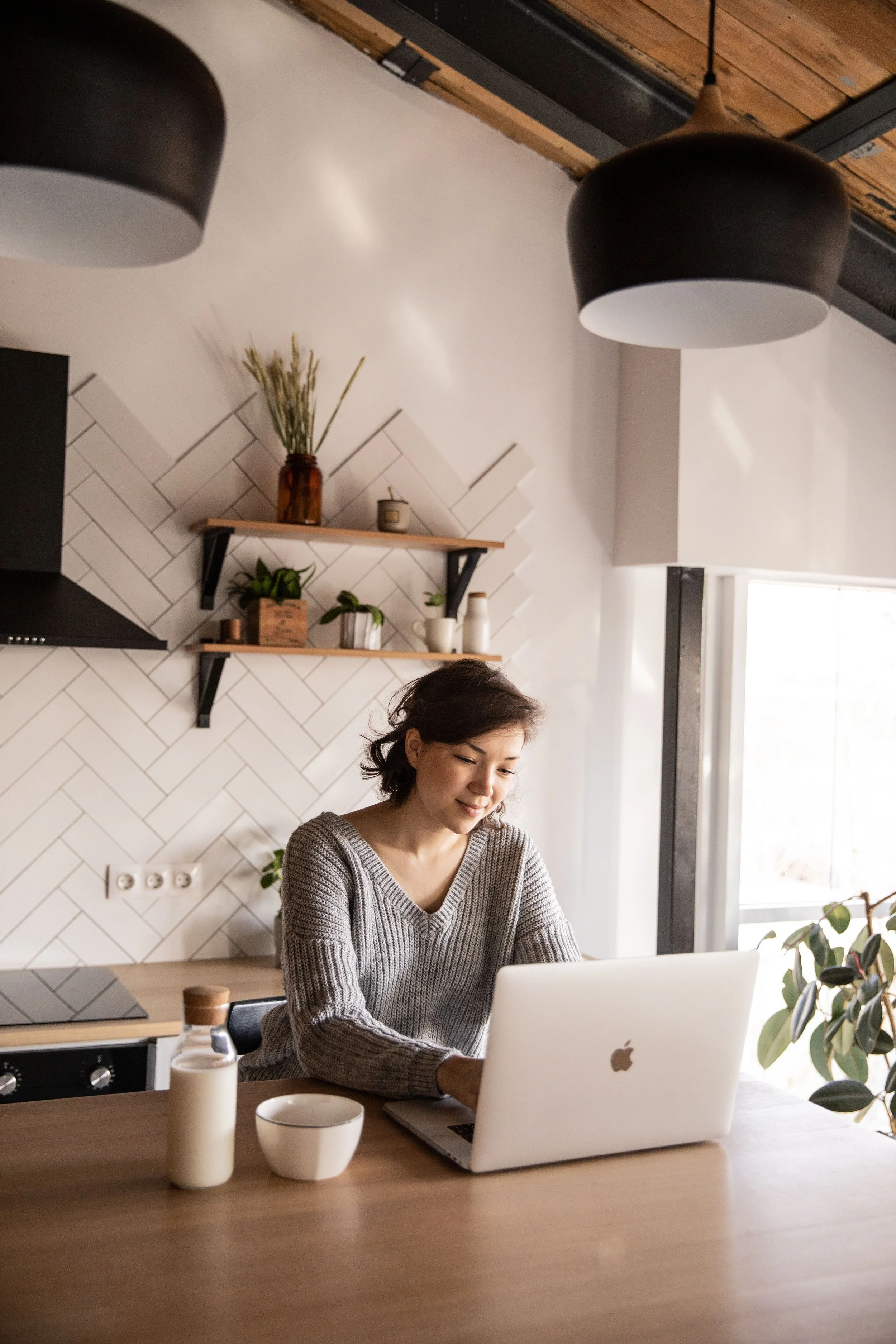 Woman working on a laptop at a kitchen counter, representing a virtual individual therapy session