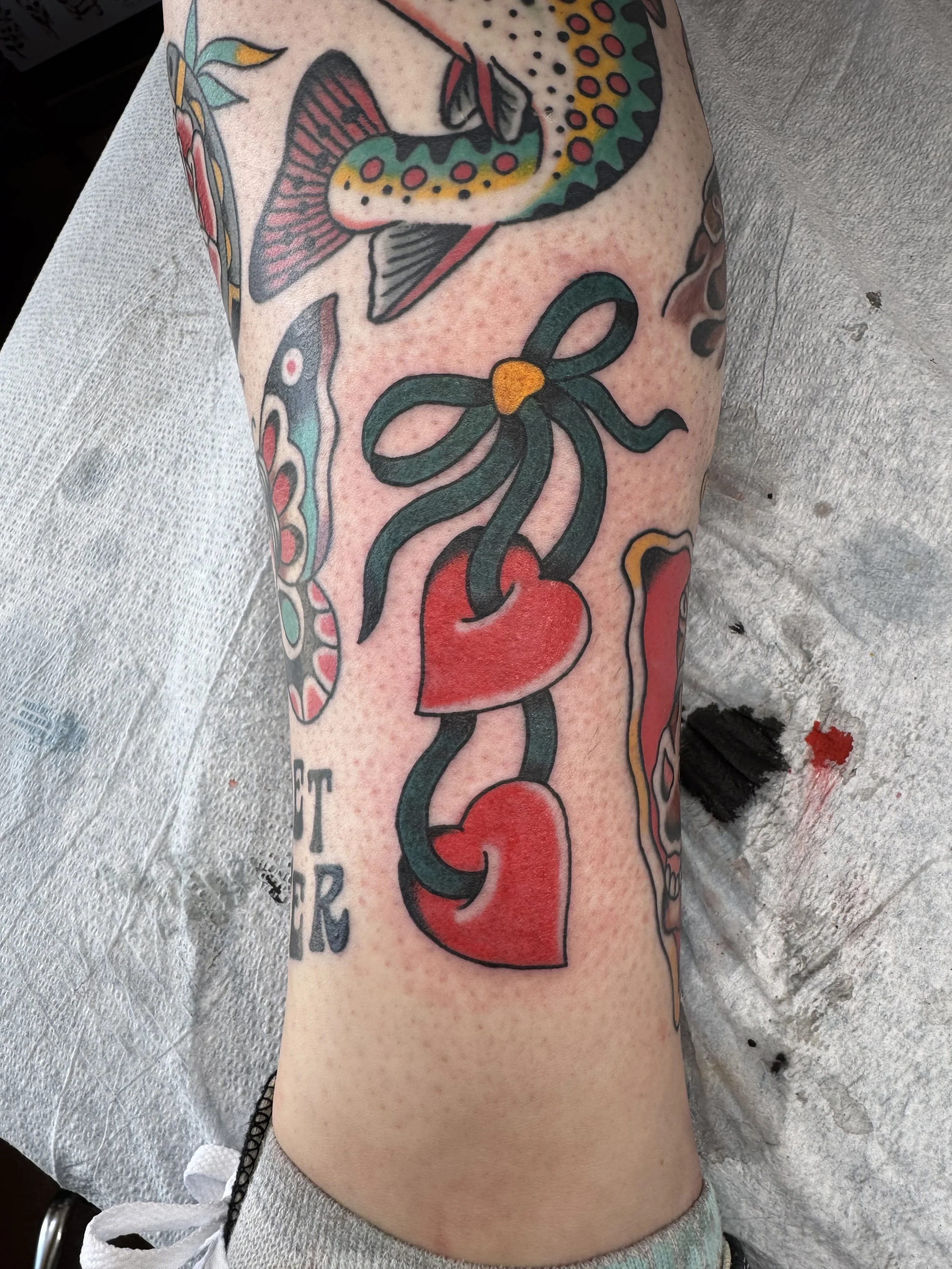 Colorful tattoo on a person's arm featuring a snake, a heart, a ribbon, and a flower with traditional tattoo style.