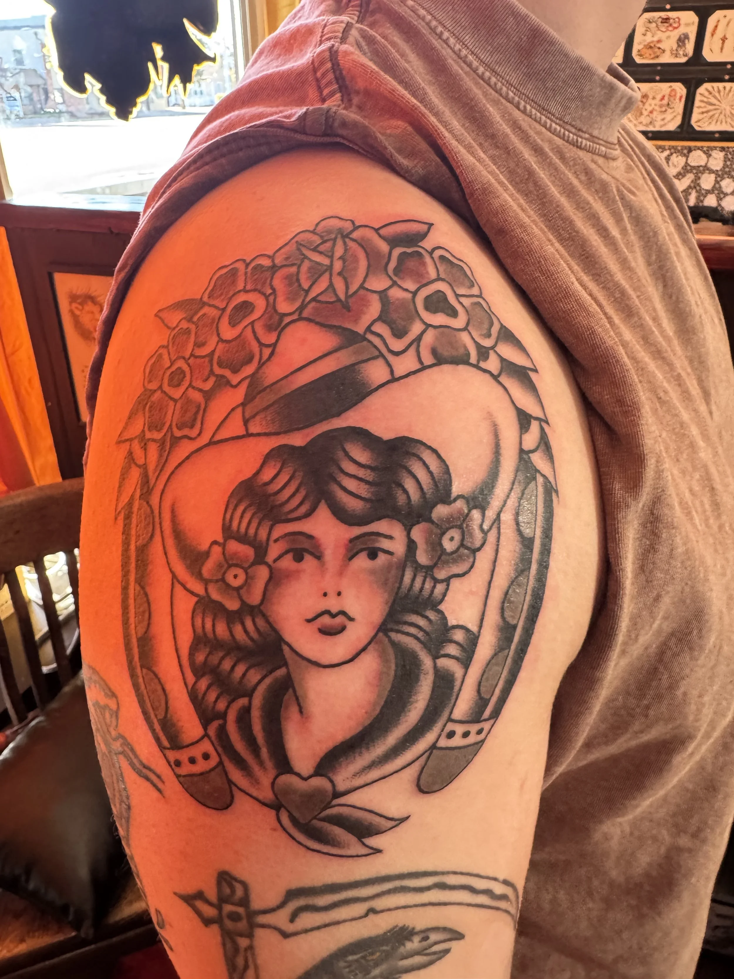 Tattoo of a woman with flowers in her hair on a person's upper arm, in black ink with detailed shading.