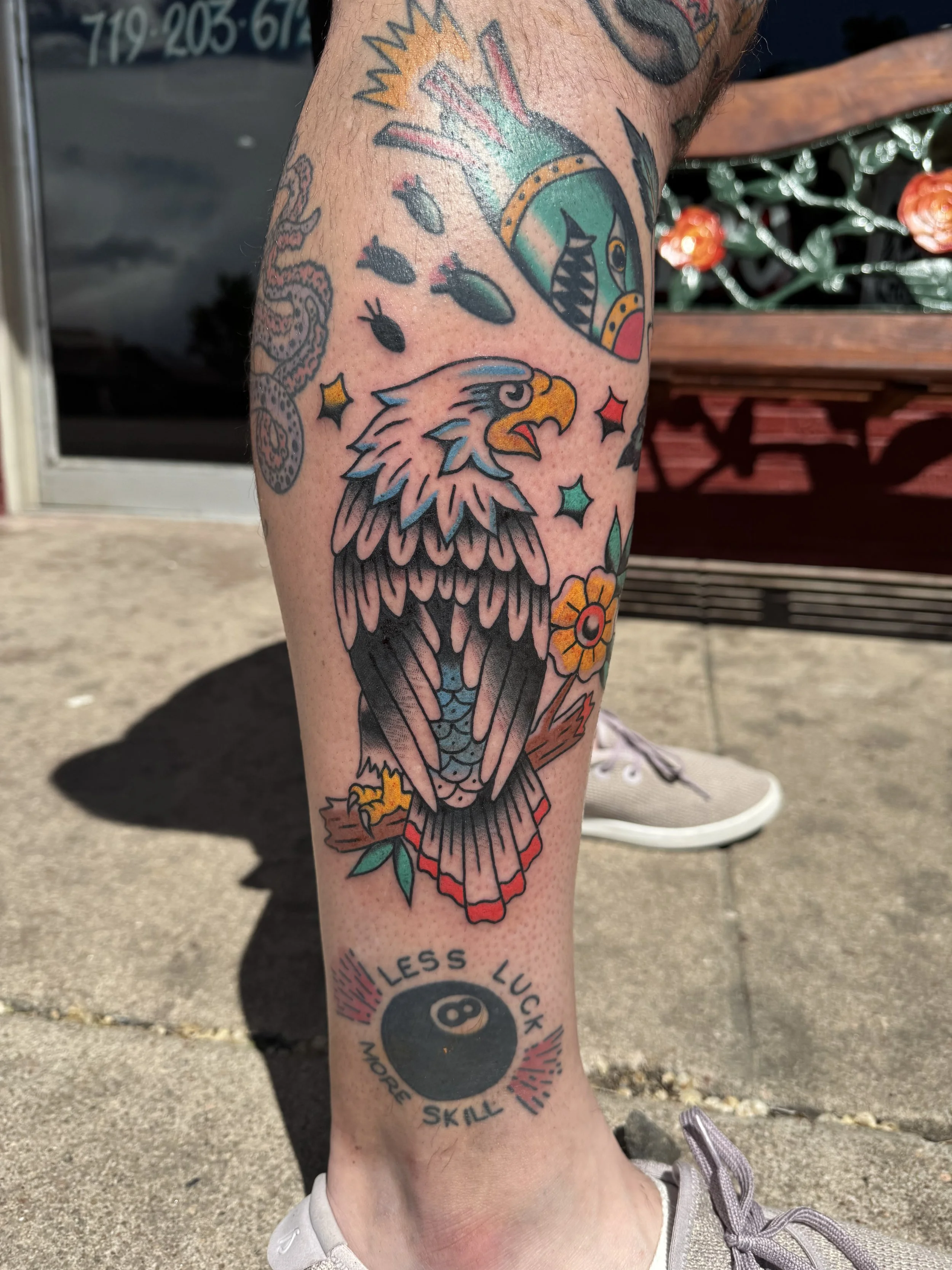 Tattoo of an eagle with detailed feathers on a person's leg, surrounded by stars and various small designs.