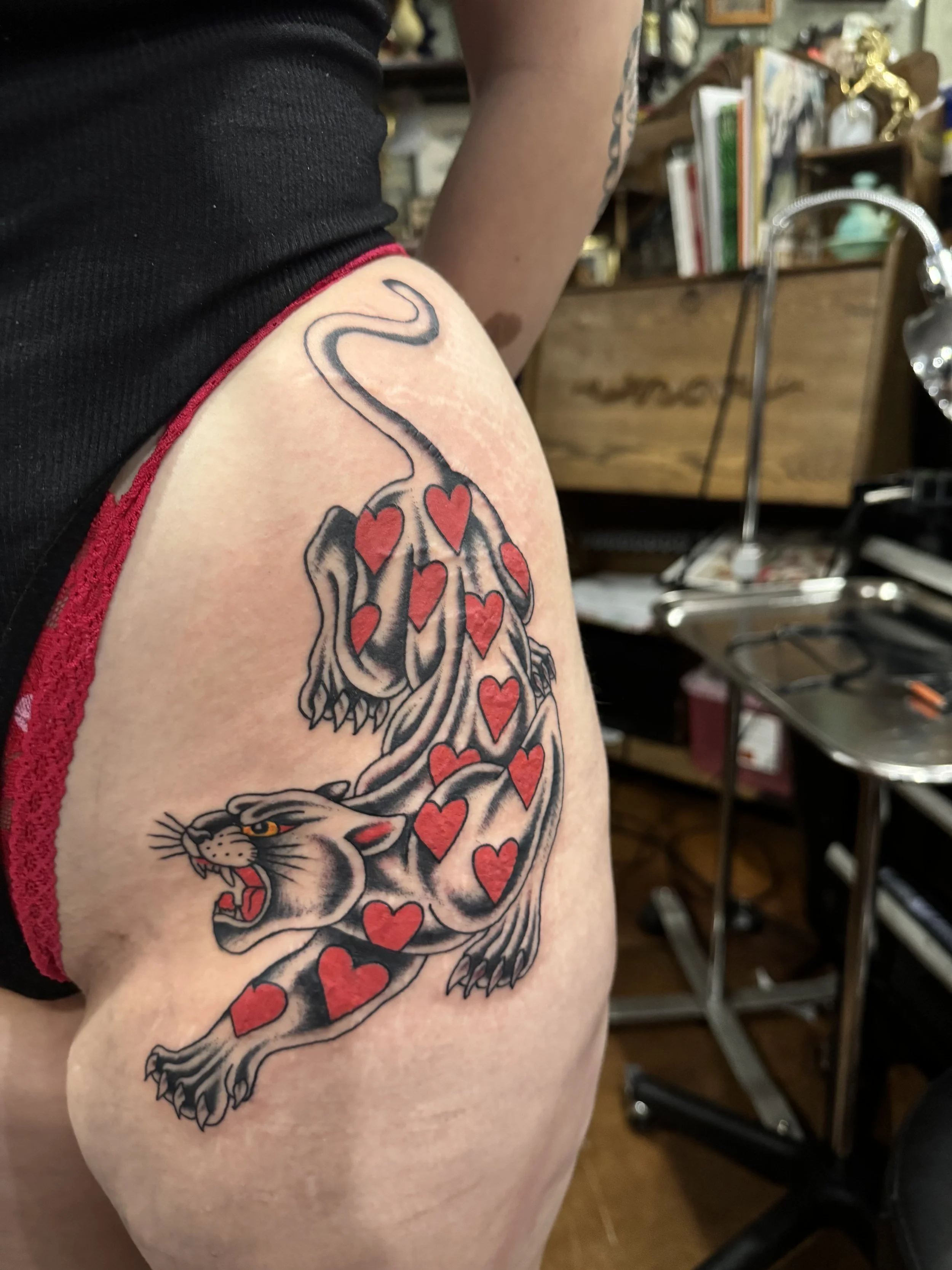 Tattoo of a snarling panther with red hearts on its body on a person's upper arm and shoulder.