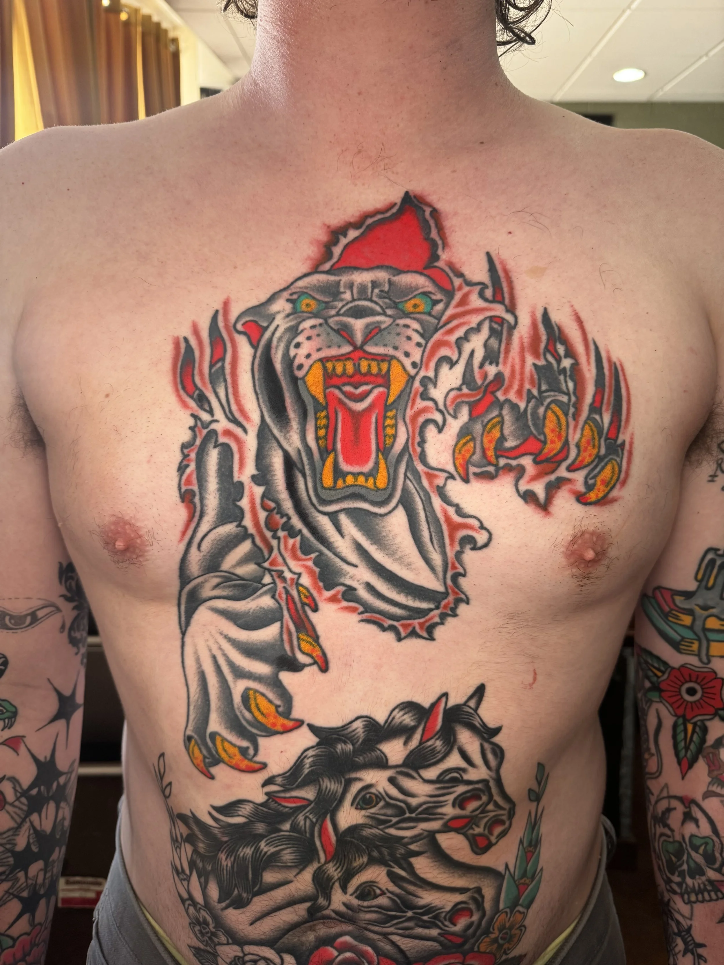 Tattoo of a roaring lion's head on a person's chest with flames and design elements around it.