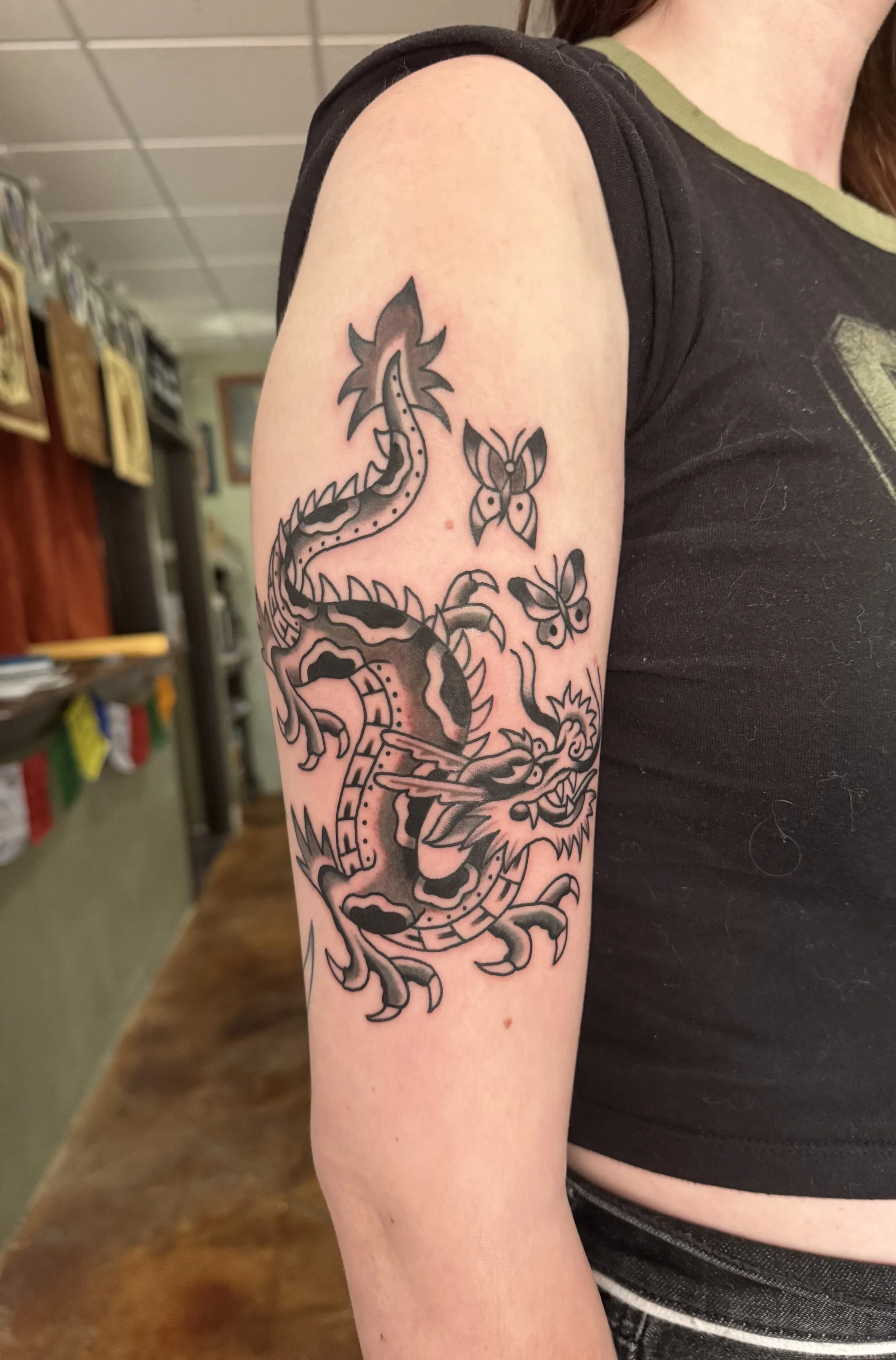 A tattoo of a dragon on a person's upper arm, with butterflies surrounding it.