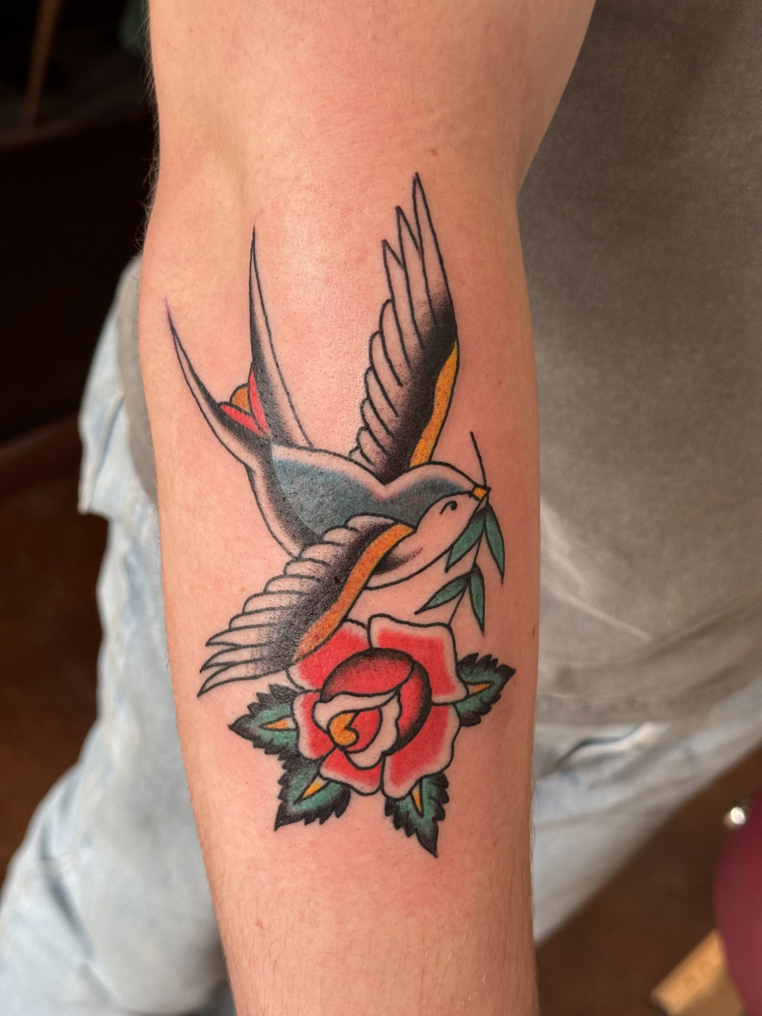 Tattoo of a colorful bird holding a red rose on a person's arm.