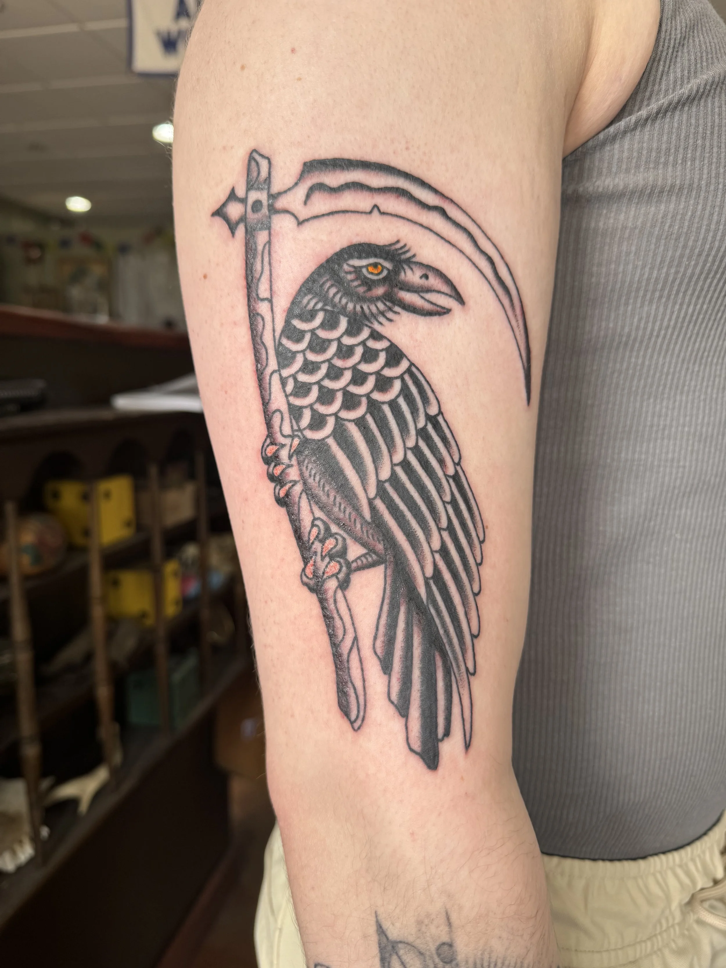 Tattoo of a raven with an eye, holding an axe with a wavy blade.