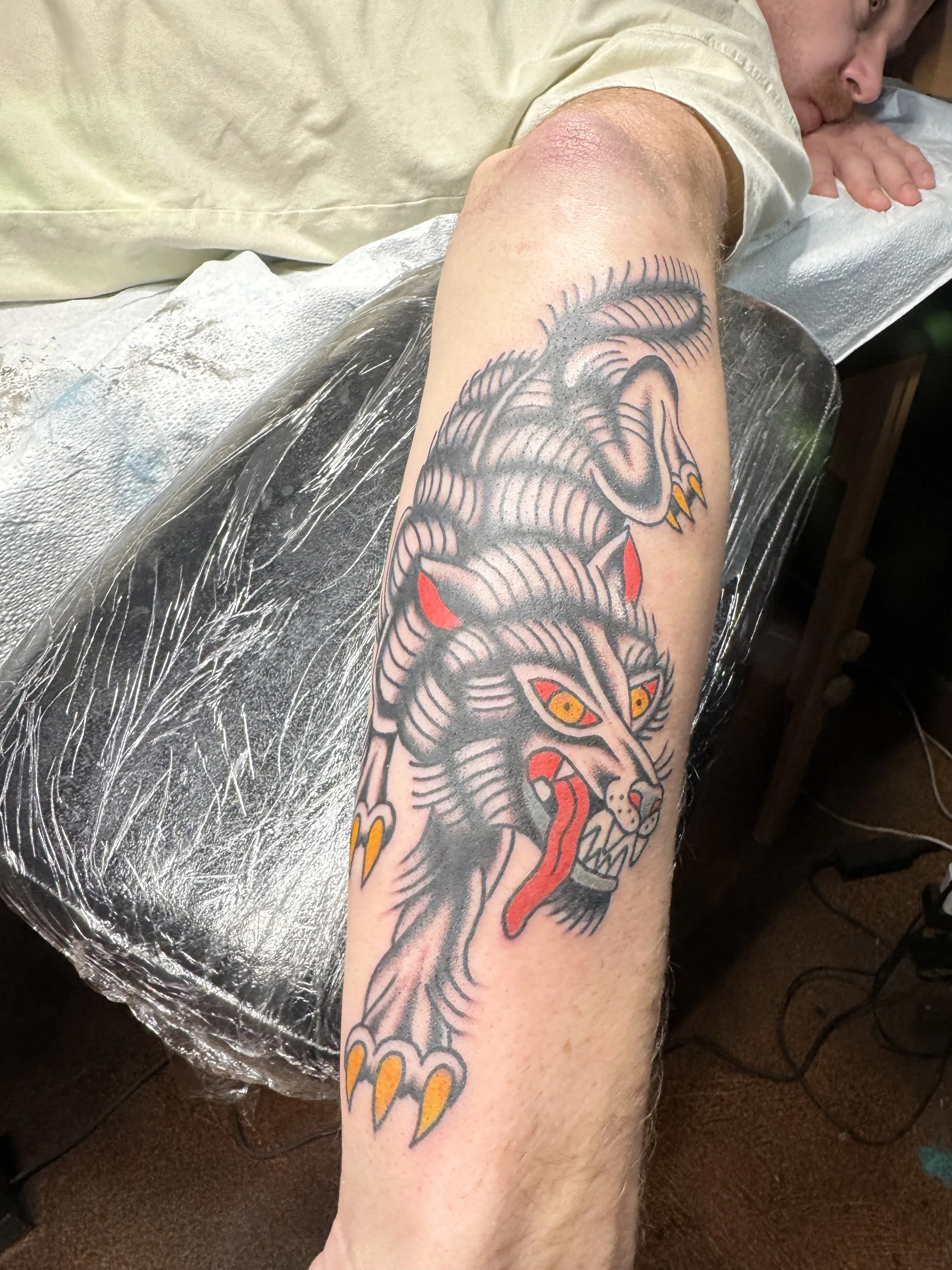 A person's upper arm with a tattoo of a fierce dragon with yellow eyes, red tongue, and detailed line work.