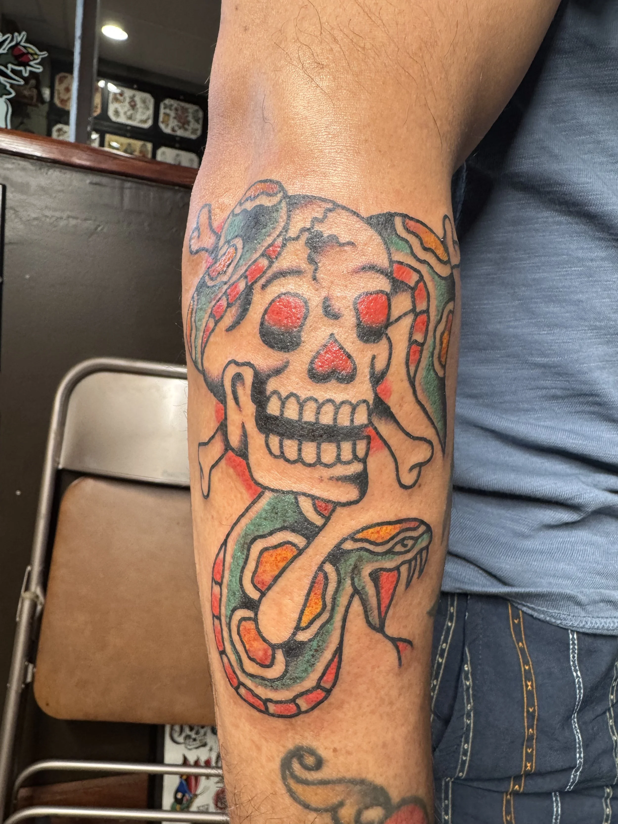Tattoo of a colorful skull with a snake wrapped around it on a person's arm.