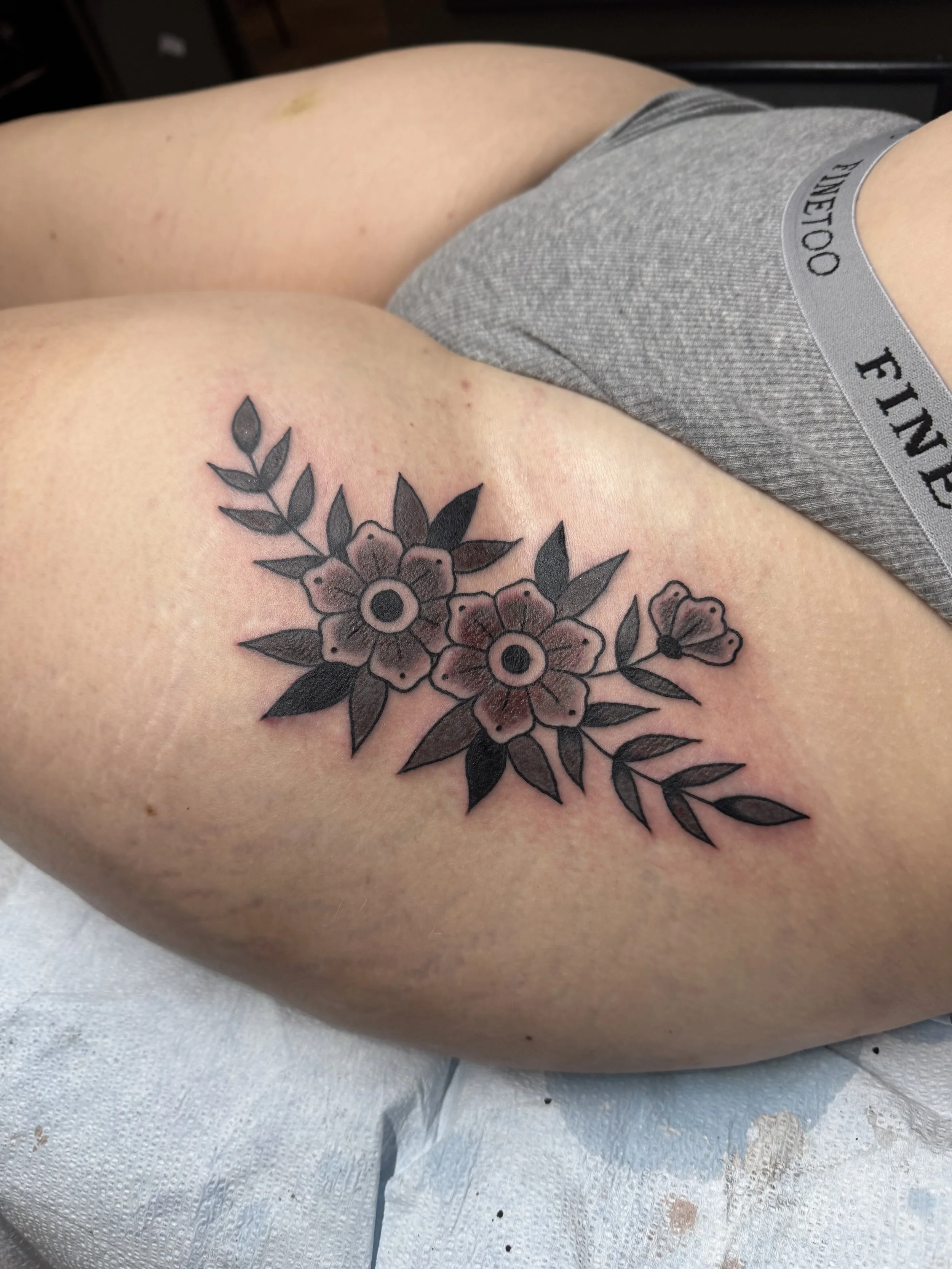 Tattoo of blackout flowers and leaves on person's upper thigh.