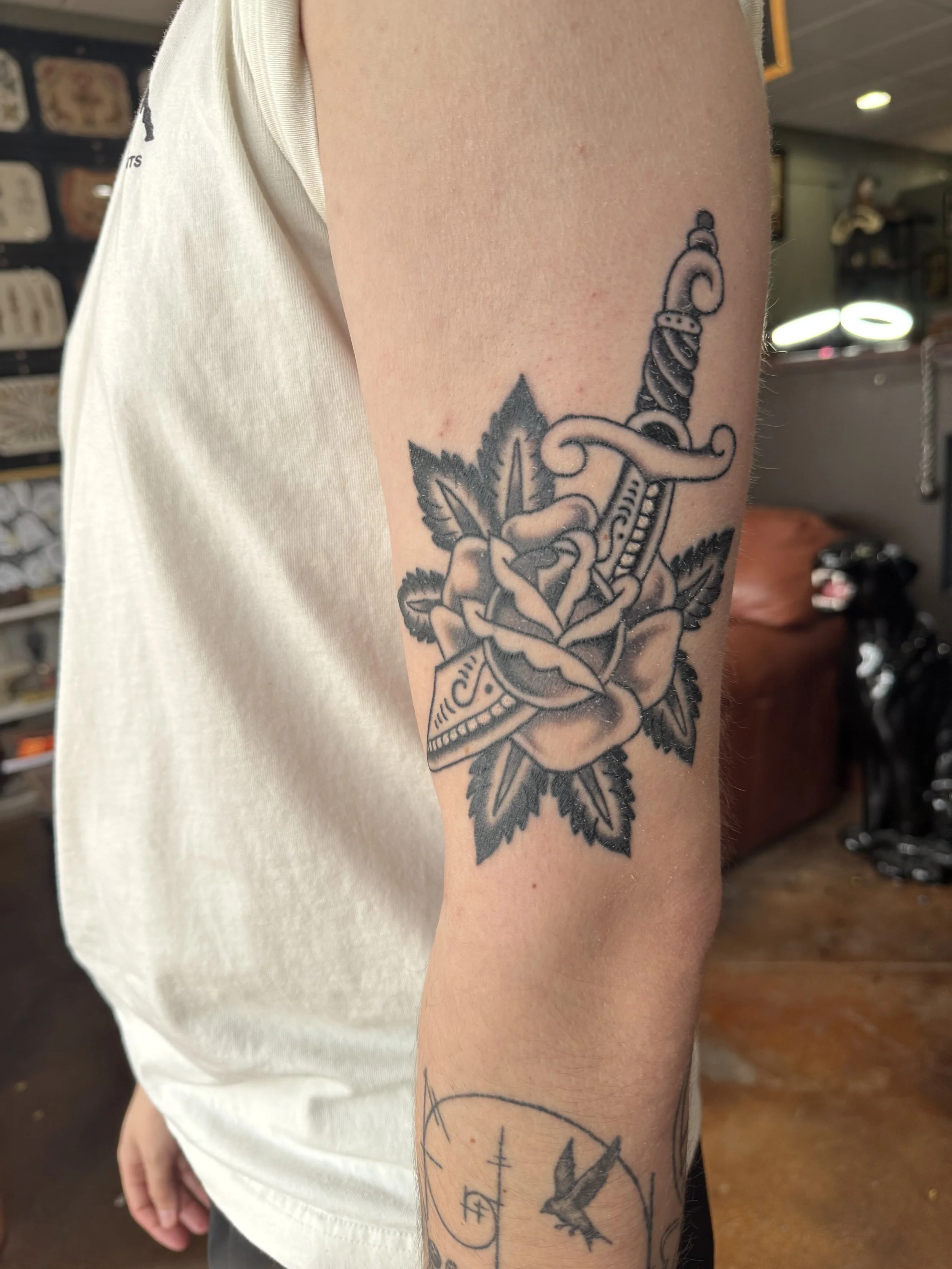 Tattoo of a dagger piercing a rose on a person's upper arm.
