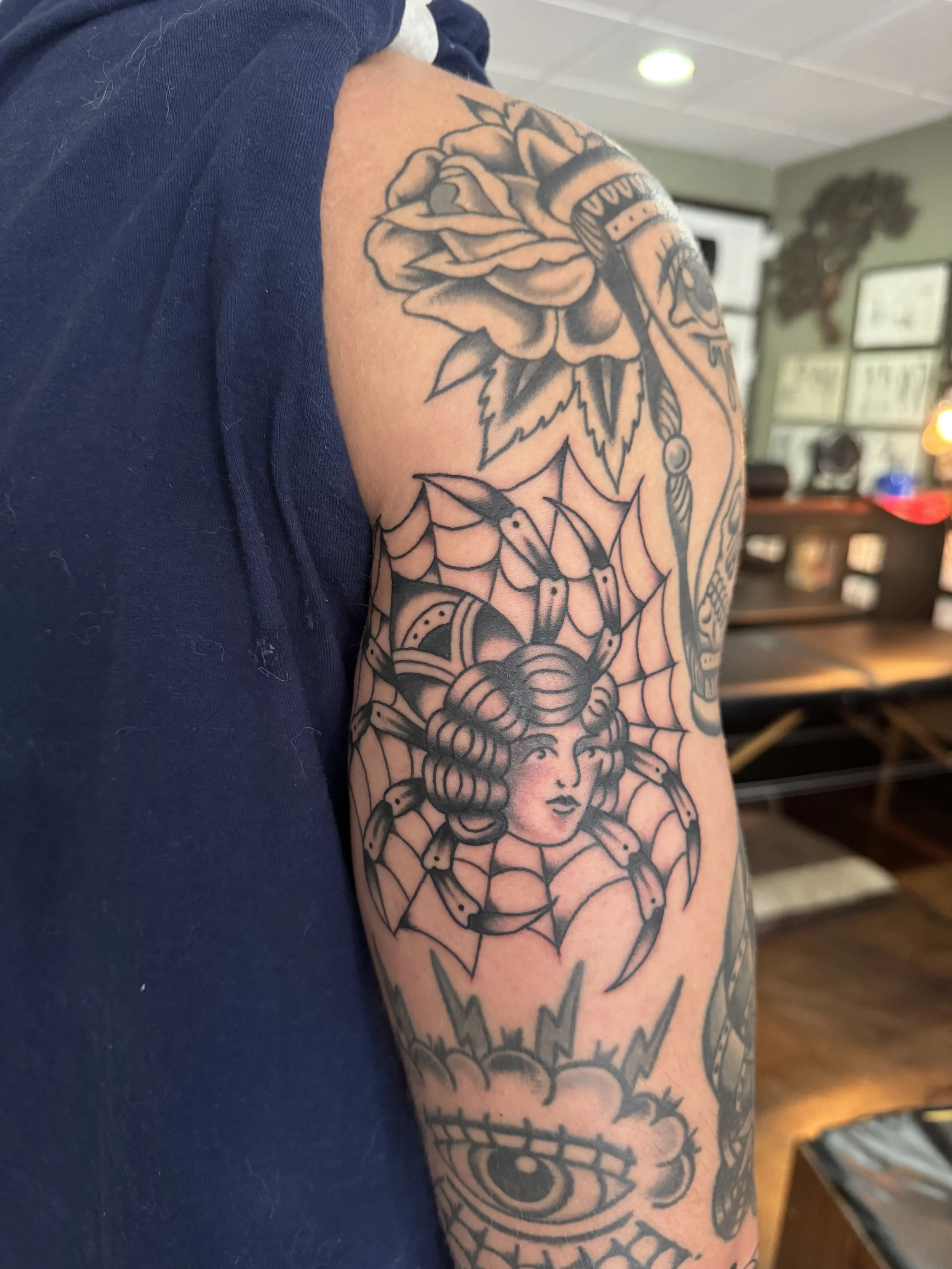 Tattoo of a woman's face with braided hair and a spider web on her shoulder, located on a person's upper arm.