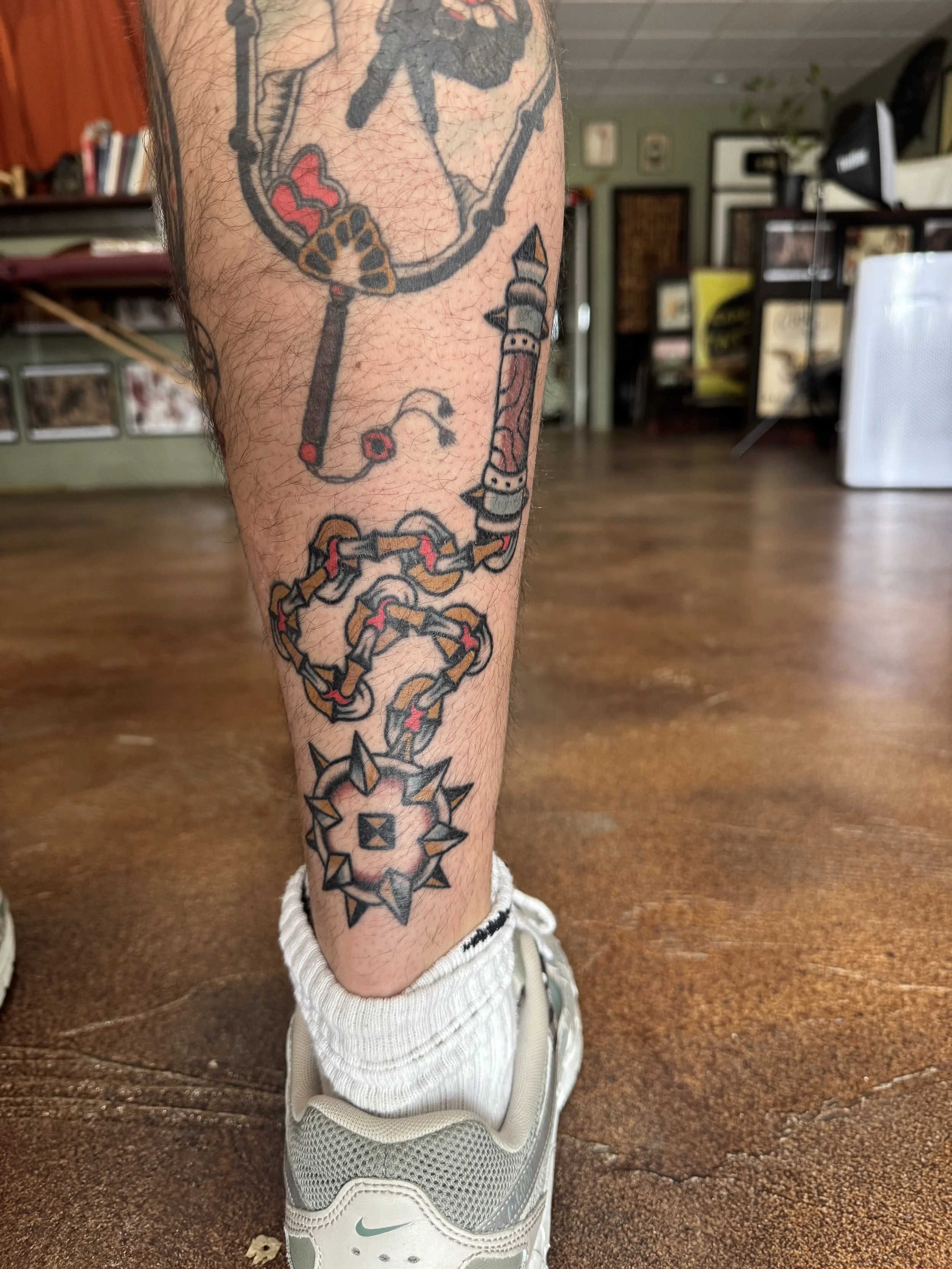 Tattooed leg in sneaker with tattoos including a dreamcatcher and chain designs.