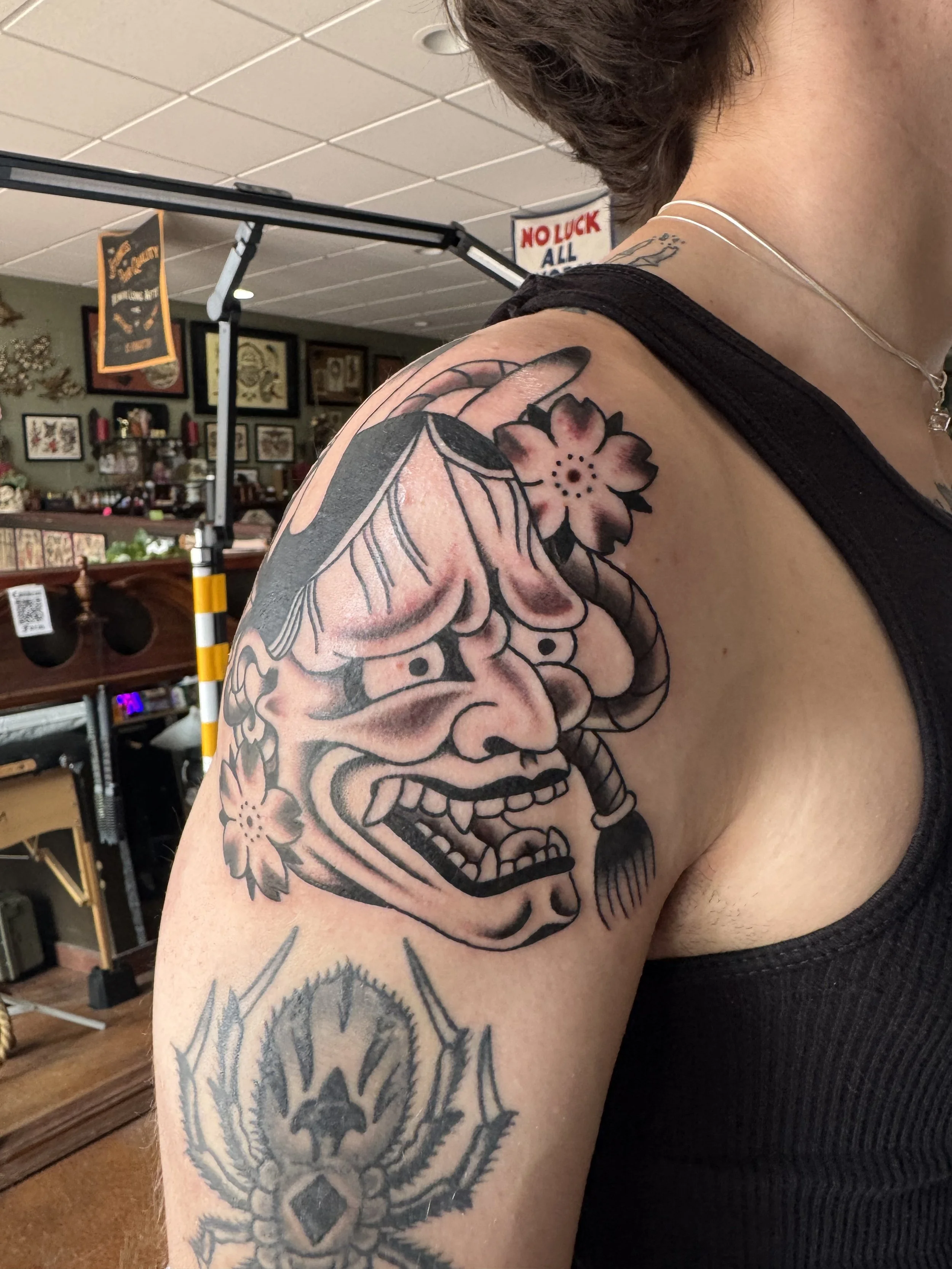 Close-up of a person's upper arm and shoulder with a large tattoo of a traditional-style skull with flowers and leaves.