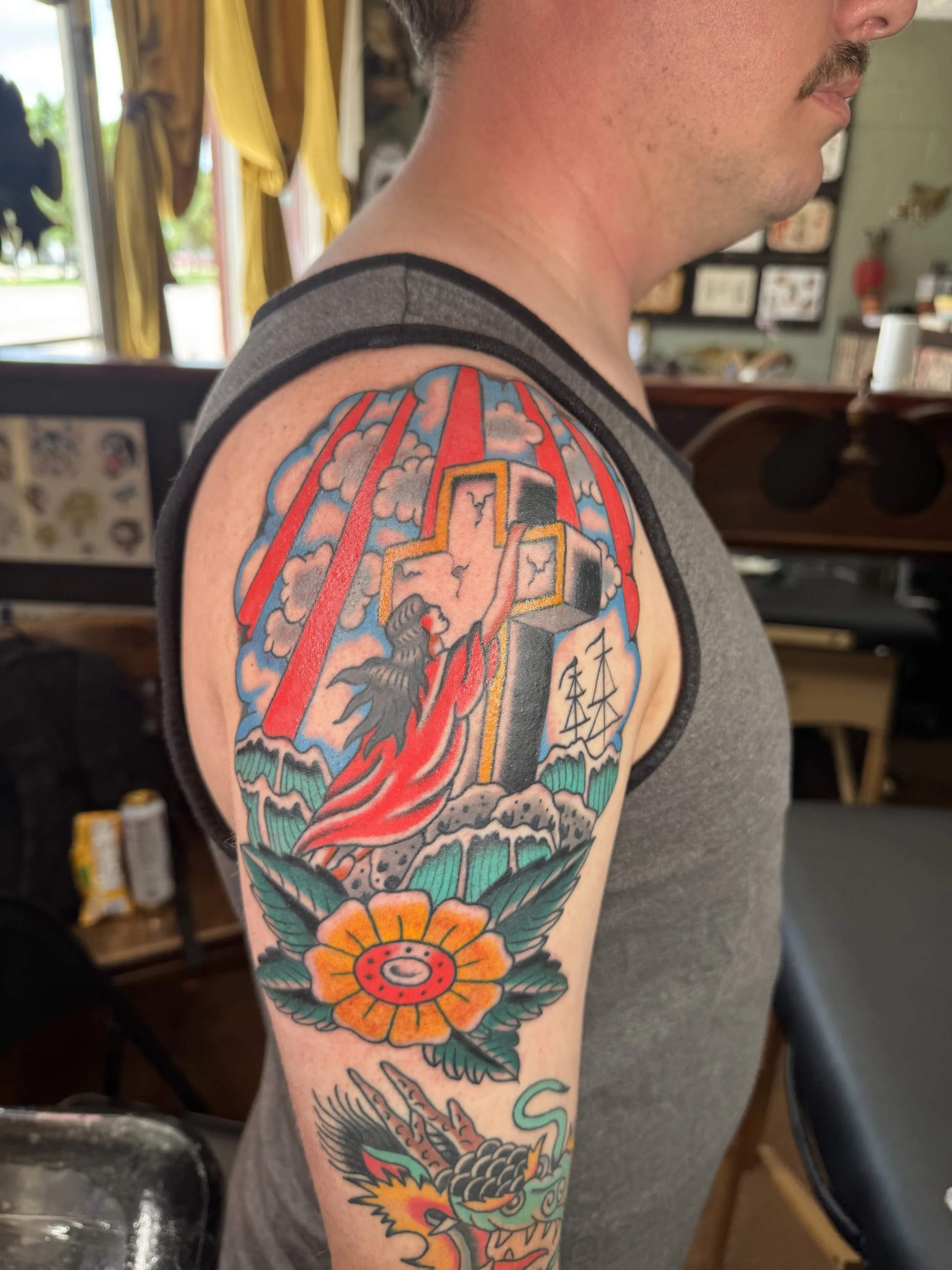 Colorful tattoo on man's upper arm featuring a dragon, cloud, sun, traditional Japanese elements, vibrant colors, and bold outlines.