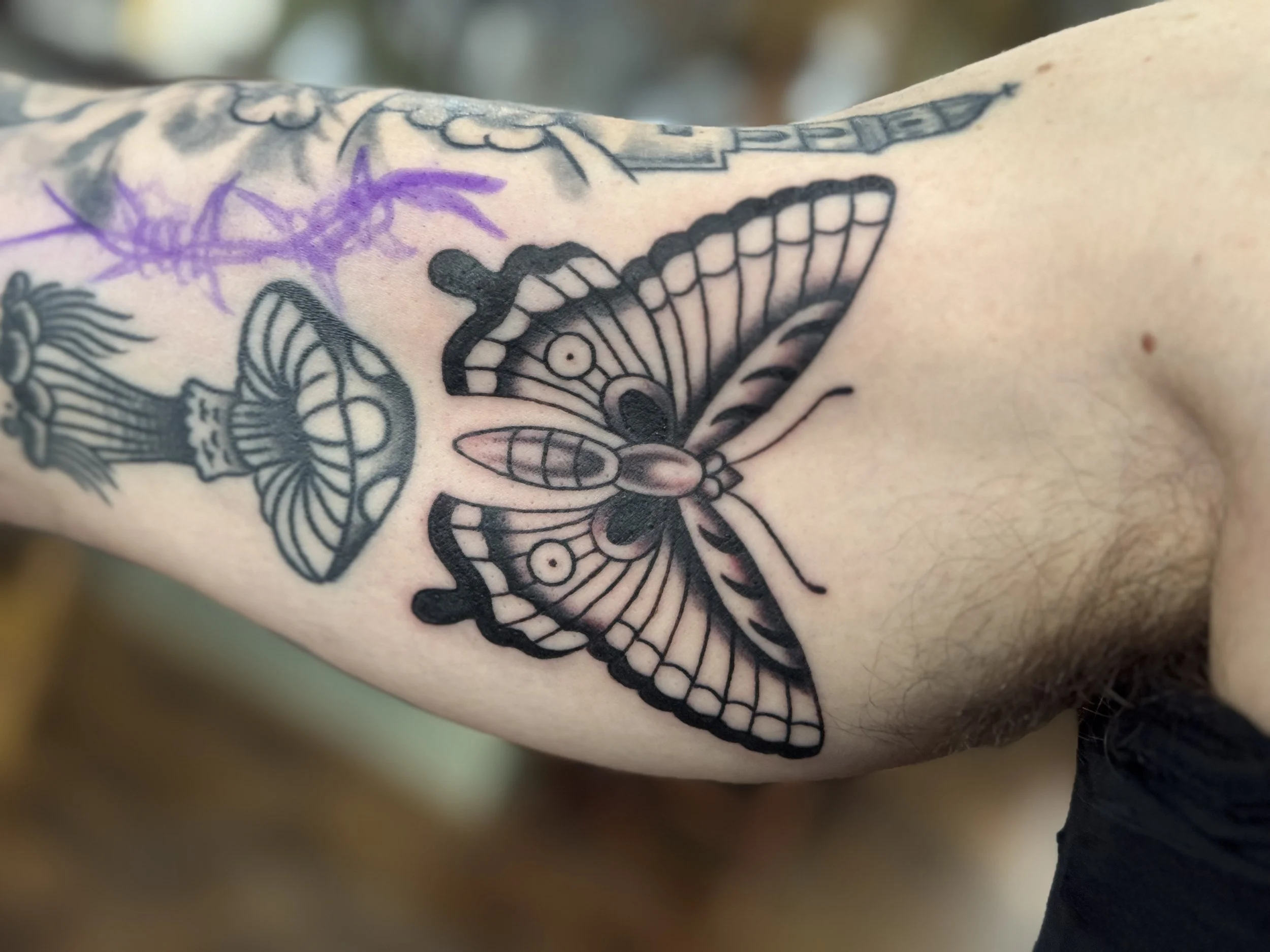 Close-up of a person's forearm with various tattoos, including a butterfly and purple ink streaks.