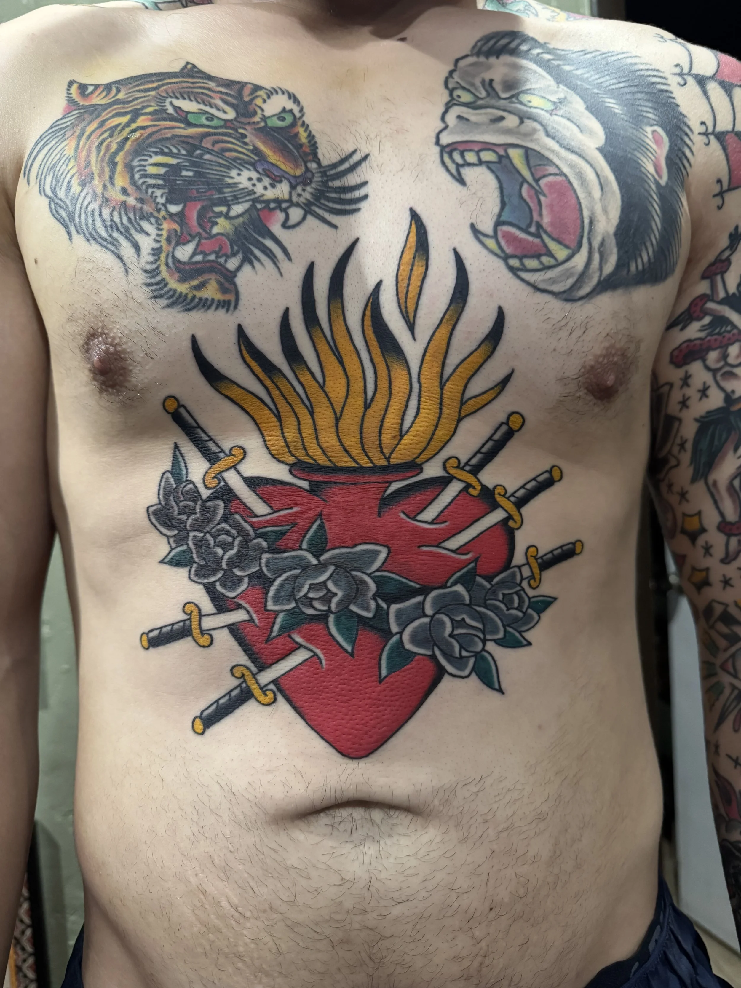 Tattoo of a roaring tiger and a roaring gorilla facing each other on a person's chest with a flaming heart and swords.
