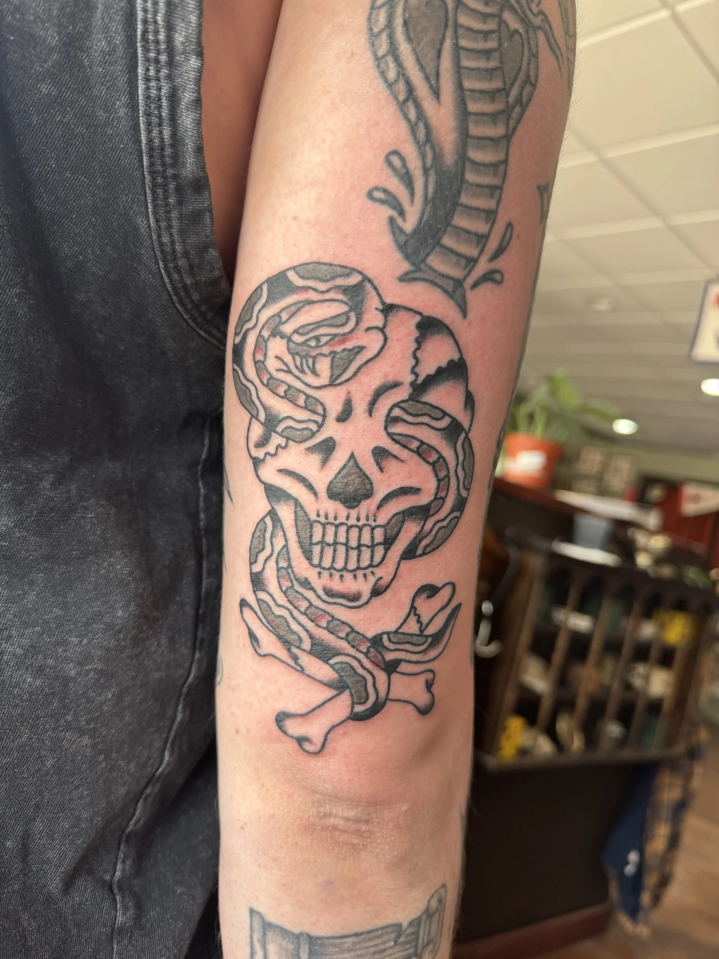 A tattoo of a skull with snake-like features on a person's arm, with the person's upper arm and black shirt visible.